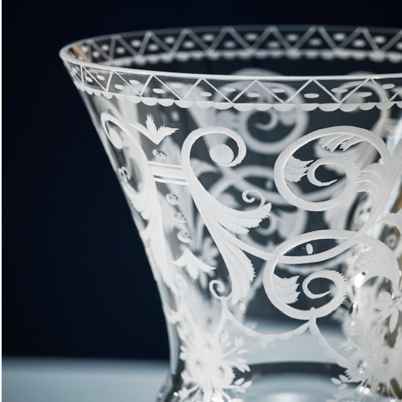 A close-up of the Lobmeyr Drinking Set No. 231 - Barock showcases intricately engraved, mouth-blown lead-free crystal against a dark background, featuring ornate swirling floral patterns and diamond lattice motifs near the rim, exemplifying Viennese Baroque craftsmanship.