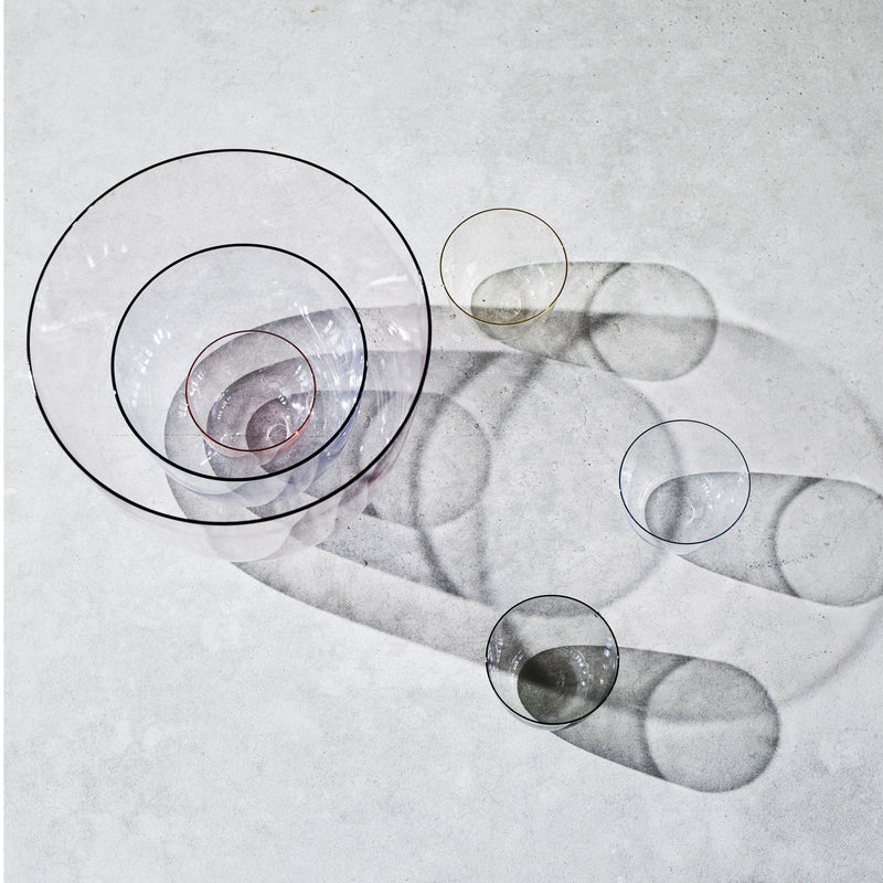 Overhead view of six Alpha Water Tumblers by Lobmeyr, crafted from mouth-blown lead-free crystal, casting shadows on a light gray surface. Arranged in descending size from top left to bottom right, these stackable pieces create intricate overlapping patterns with their delicate form.