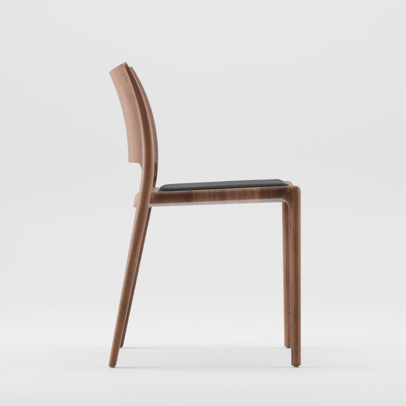 Side view of the Artisan LATUS Chair Upholstered, crafted with solid wood featuring a curved backrest and slim, straight legs. The padded seat contrasts with the natural finish. It uses eco-friendly materials, and its sleek design stands out against a plain white background.