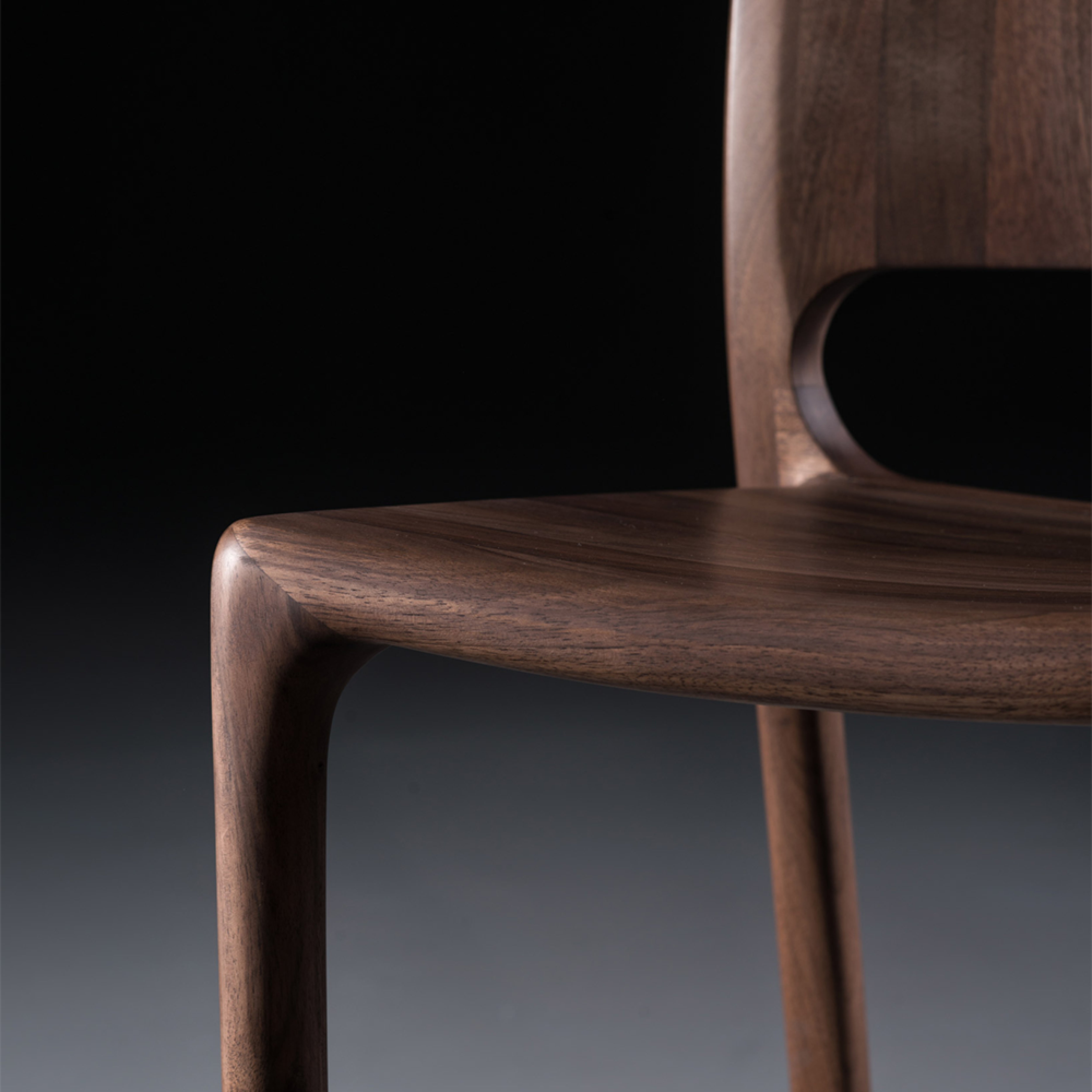 A close-up of the LATUS Chair Upholstered by Artisan reveals its smooth, polished solid wood surface. The curved, ergonomic seat and backrest are set against a dark background, emphasizing the chairs rich grain and sleek design crafted with environmentally-friendly materials.