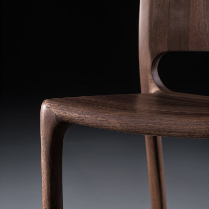 A close-up of the LATUS Chair Upholstered by Artisan reveals its smooth, polished solid wood surface. The curved, ergonomic seat and backrest are set against a dark background, emphasizing the chairs rich grain and sleek design crafted with environmentally-friendly materials.