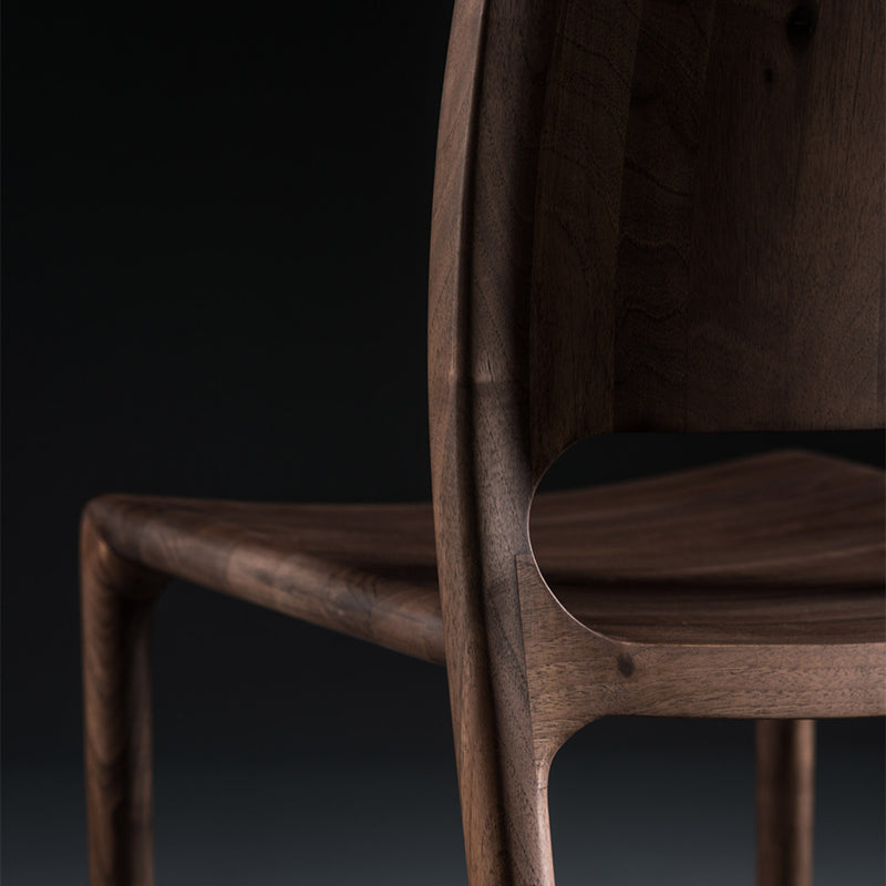 Close-up of the LATUS Chair Upholstered by Artisan, features smooth curves and rich grain in solid wood, enhanced with natural oils against a dark background.