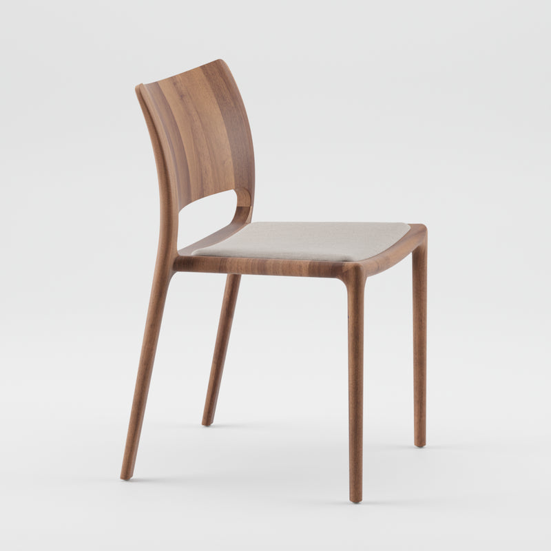 The LATUS Chair Upholstered by Artisan is a sleek, minimalist wooden chair featuring a curved backrest and cushioned seat. Its modern design is enhanced with a natural wood finish using natural oils, set against a plain white background.