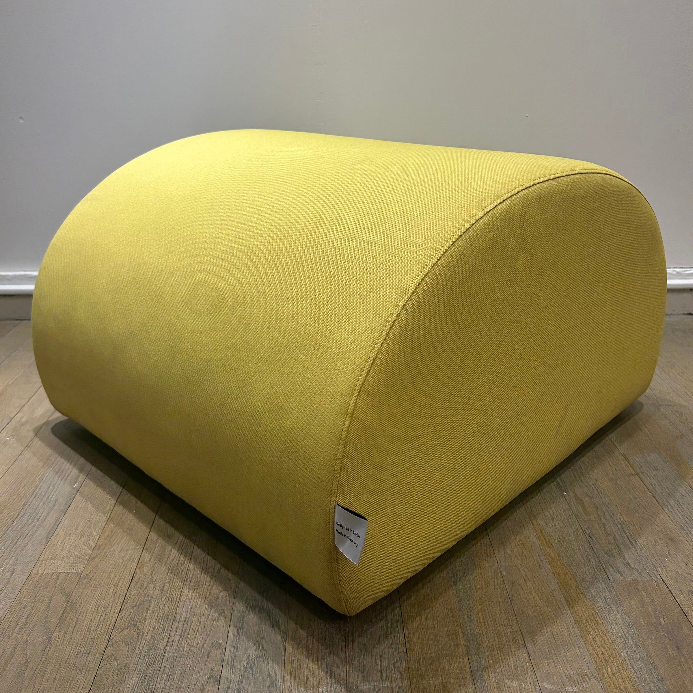 Yellow organic-shaped upholstered Levi Pouf - Sale with plywood frame on hardwood floor background.