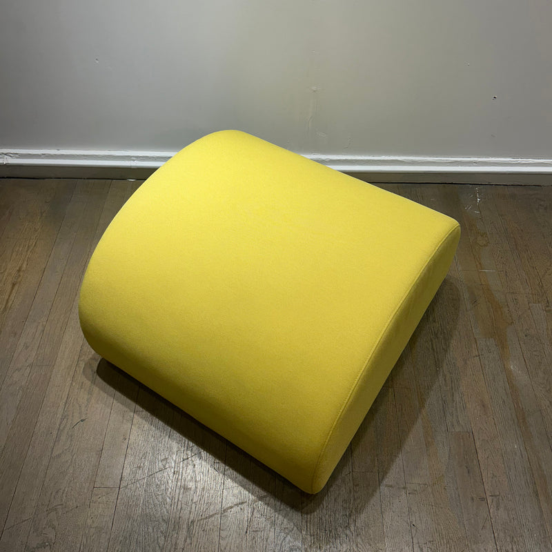 Levi Pouf - Sale bright yellow curved upholstered seating object on wooden floor against gray wall.