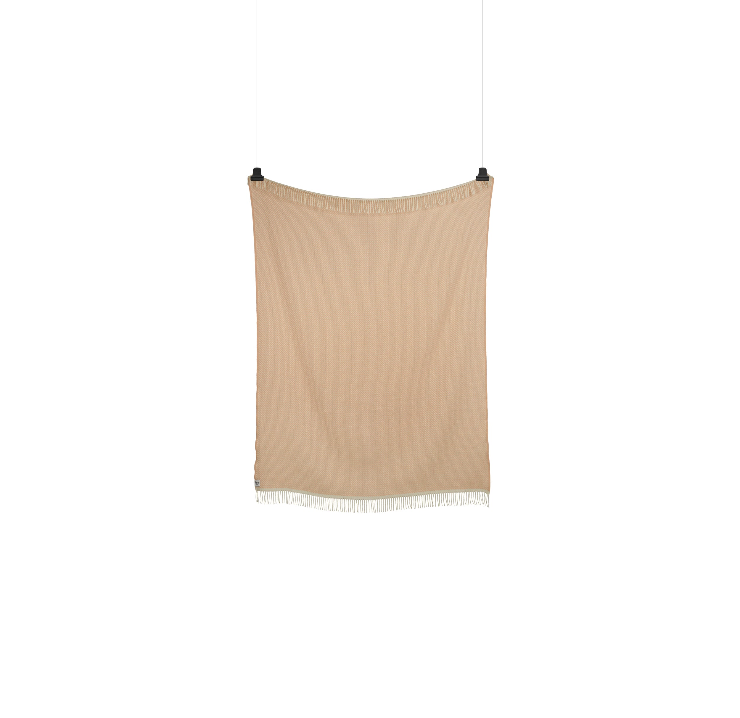 A MELLO Throw from Roros in beige with a white fringe, crafted from luxurious Norwegian lambswool, is elegantly suspended by two black clips against a pristine white background.