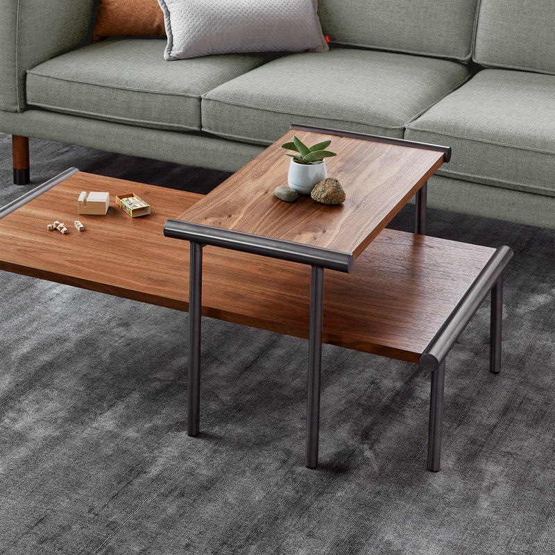 A modern living room with a gray sofa and the Gus Modern Manifold Coffee Table Rectangle, featuring metal legs, topped with a small plant, stacked books, and decorative stones, all set on a textured gray rug.