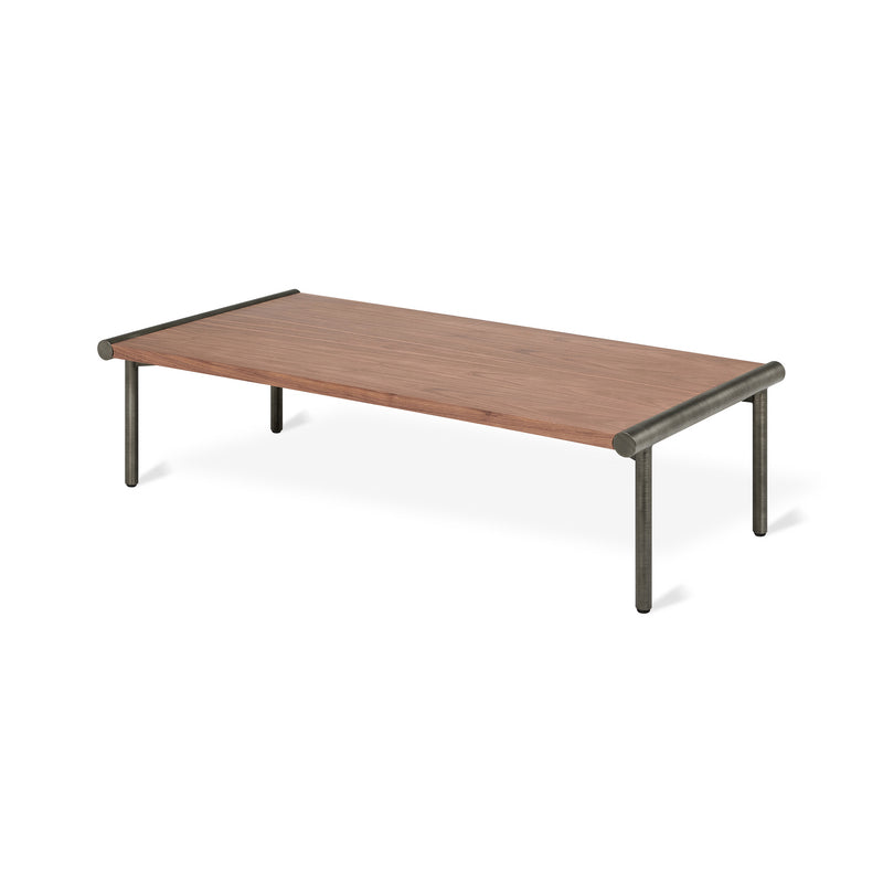 The Manifold Coffee Table Rectangle by Gus Modern features a rectangular wood top and four metal legs, showcasing a minimalist, modern industrial design inspired by Bauhaus style.