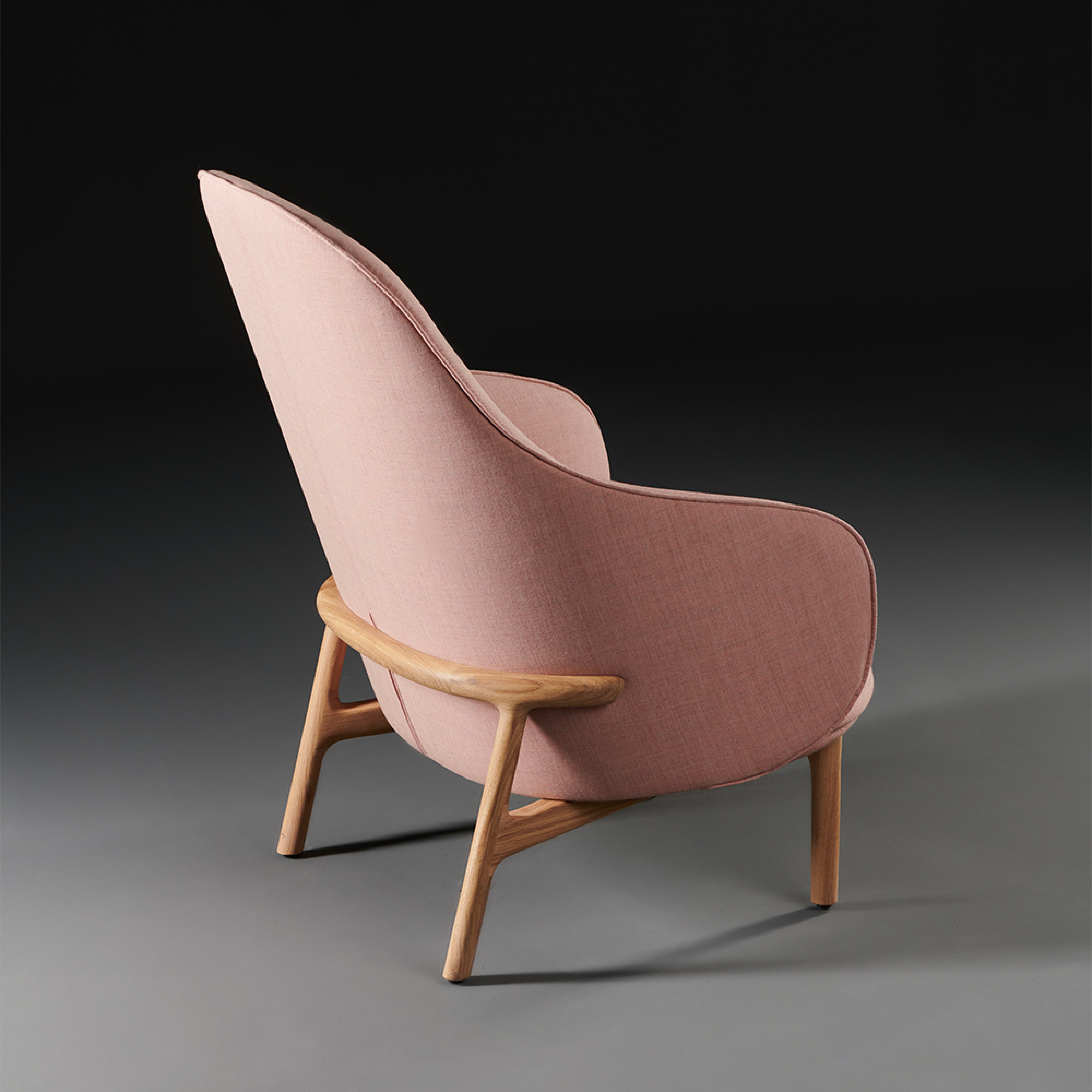 The Artisan MELA Lounge Chair High boasts a modern, sleek design with light pink fabric and a smooth wooden frame, offering mid-century charm. Its upholstered shell accentuates the elegant lines, making it a standout piece from the collection.