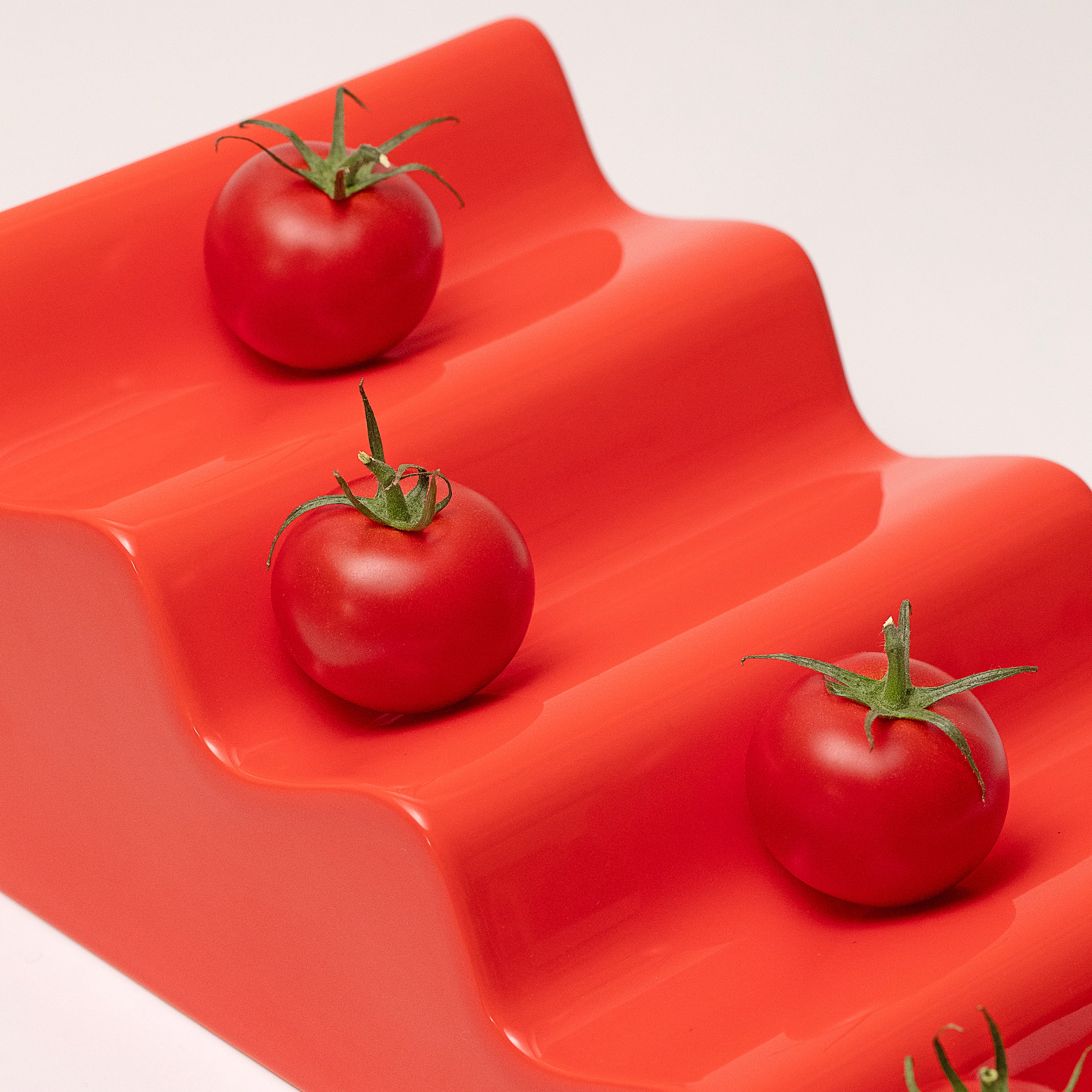CASCADE Fruitstand in glossy red ceramic with three fresh tomatoes displayed on its tiered platform.