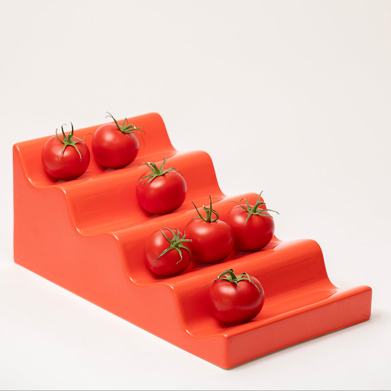 CASCADE Fruitstand in glossy red ceramic holding fresh tomatoes on tiered sections against a plain background