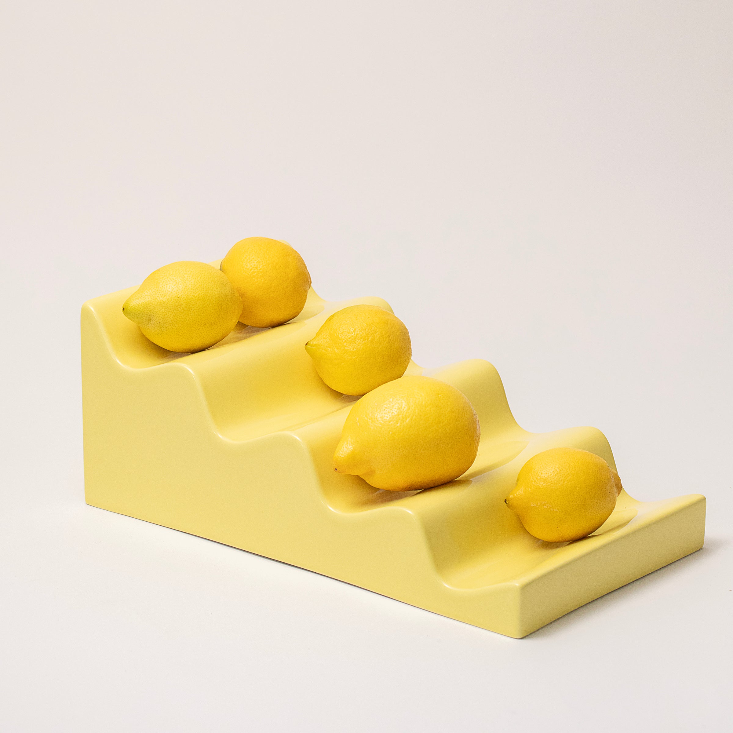 CASCADE Fruitstand in glossy yellow ceramic displaying six fresh lemons in a practical stepped design.