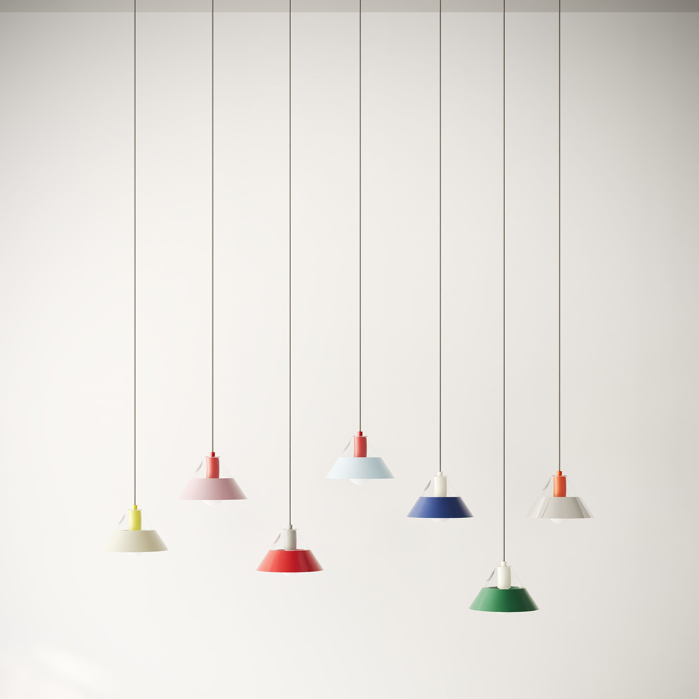 FIFTY FIFTY lamp pendant lights in various colors with glass tops and metal shades, hanging in a row against a white wall.