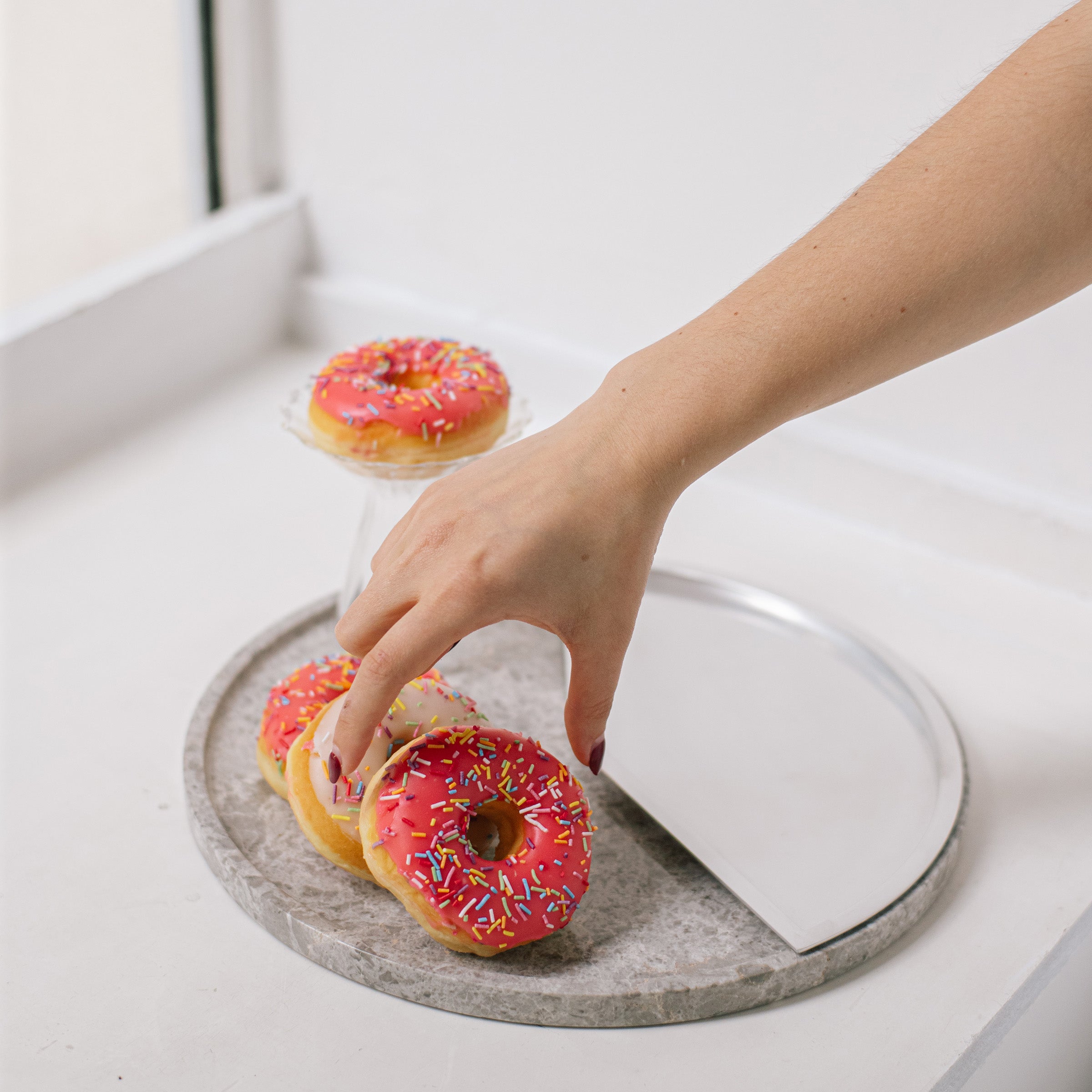 5 O'CLOCK Tray with round marble base and aluminum inlay holding three pink frosted donuts with sprinkles