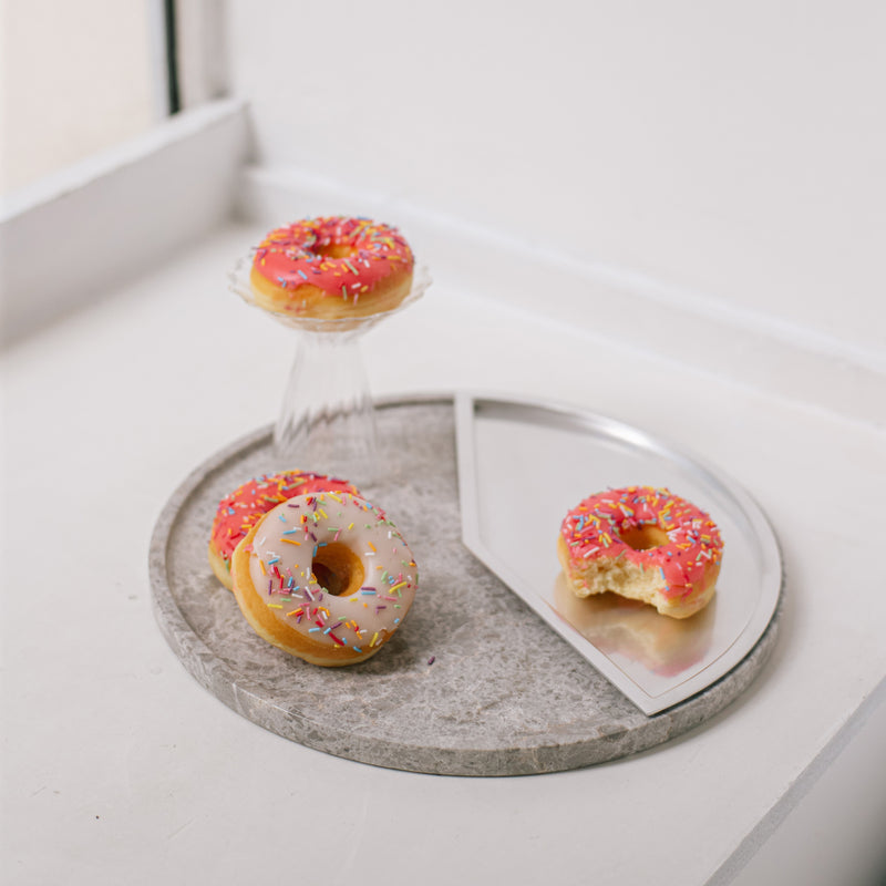 5 O'CLOCK Tray with round marble base and aluminum inlay holding colorful sprinkled donuts.