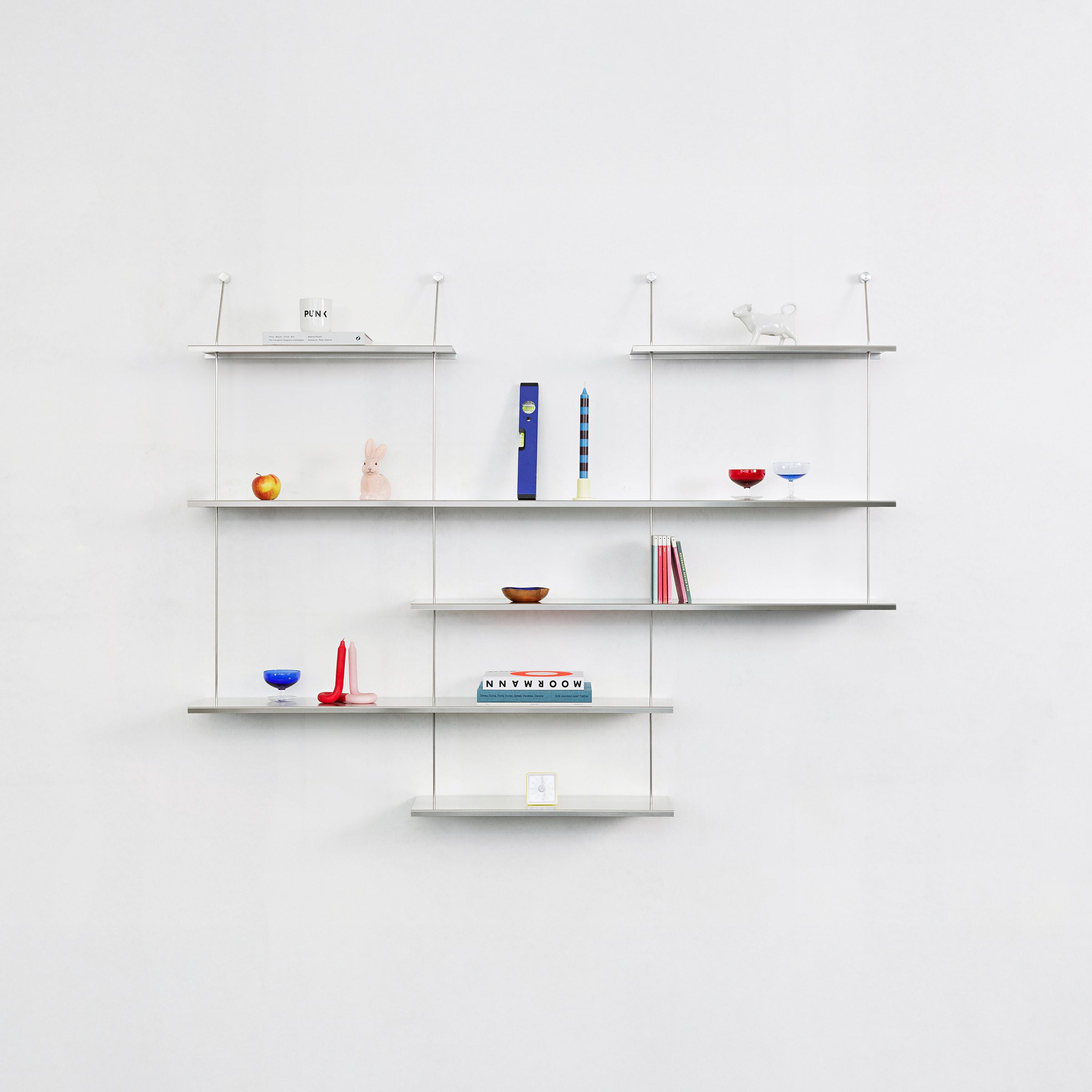 The Liesl wall-mounted shelves by Moormann display a curated selection: books, candles, a small sculpture, colorful bowls, and an apple against a pristine white background.