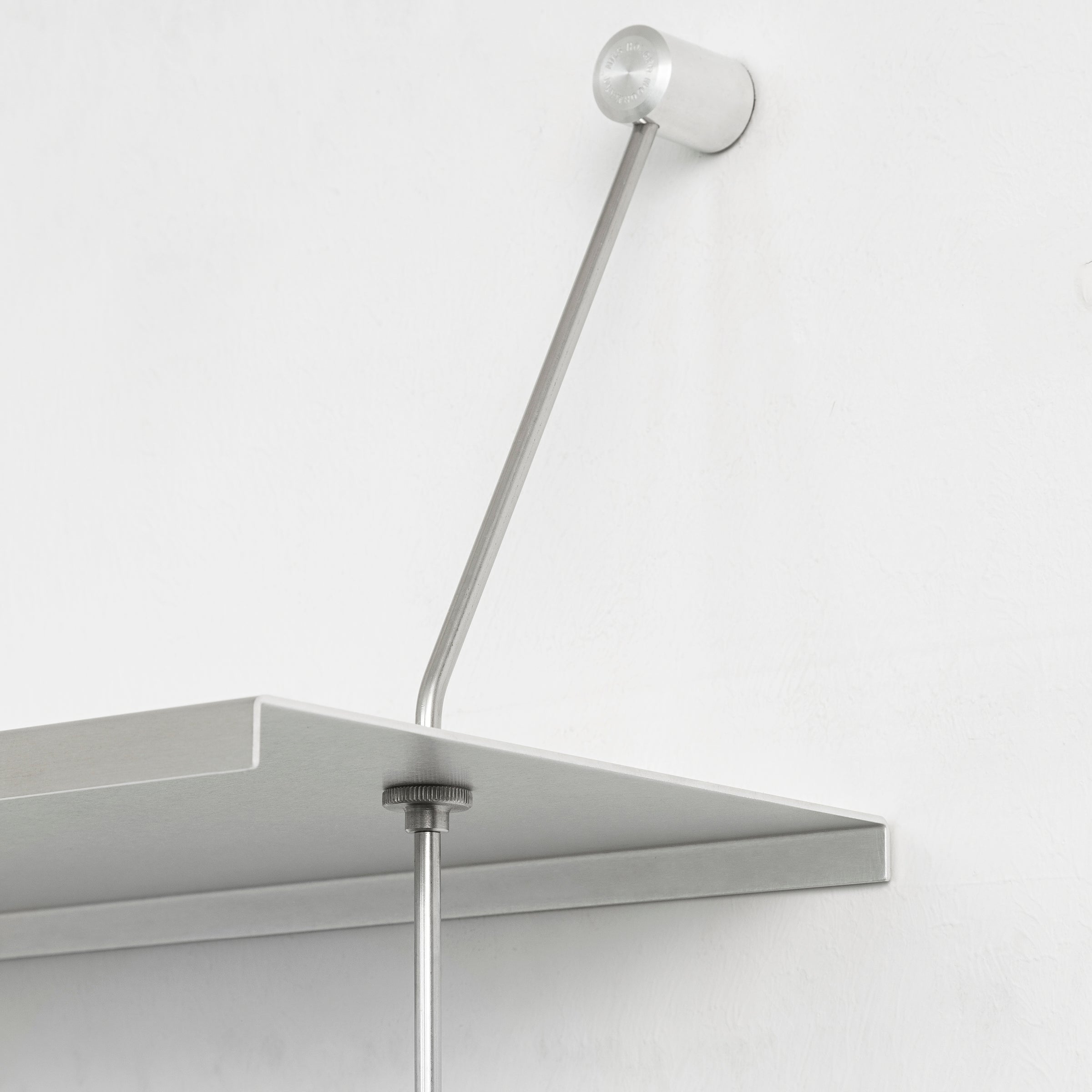A close-up of the Liesl support bracket by Moormann shows it seamlessly integrated into a modular furniture setup on a white wall. The slender rod connects the sleek metal shelf, adding a modern touch to this elegant configuration.