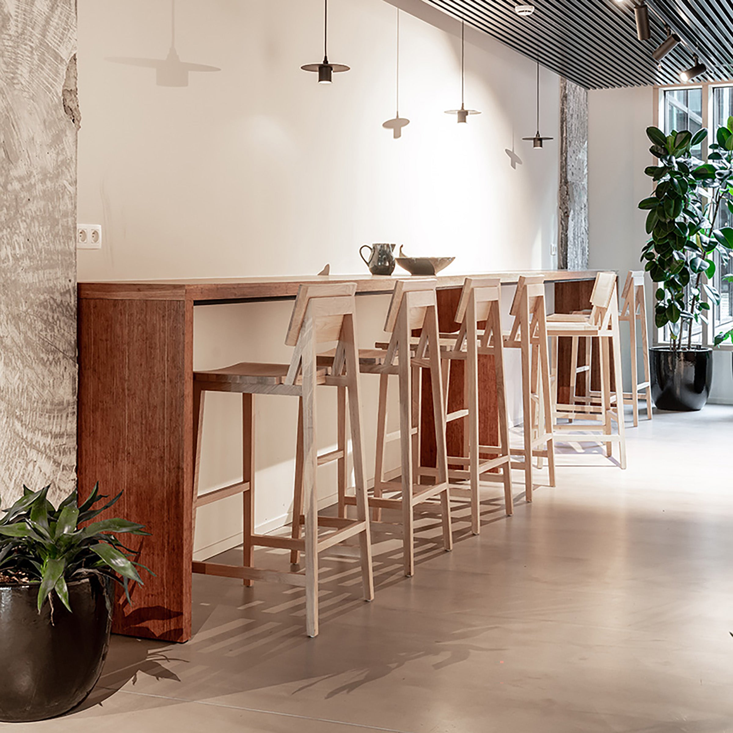 N4 Bar Stool in varnished oak arranged at a high wooden counter in a modern, bright interior space.