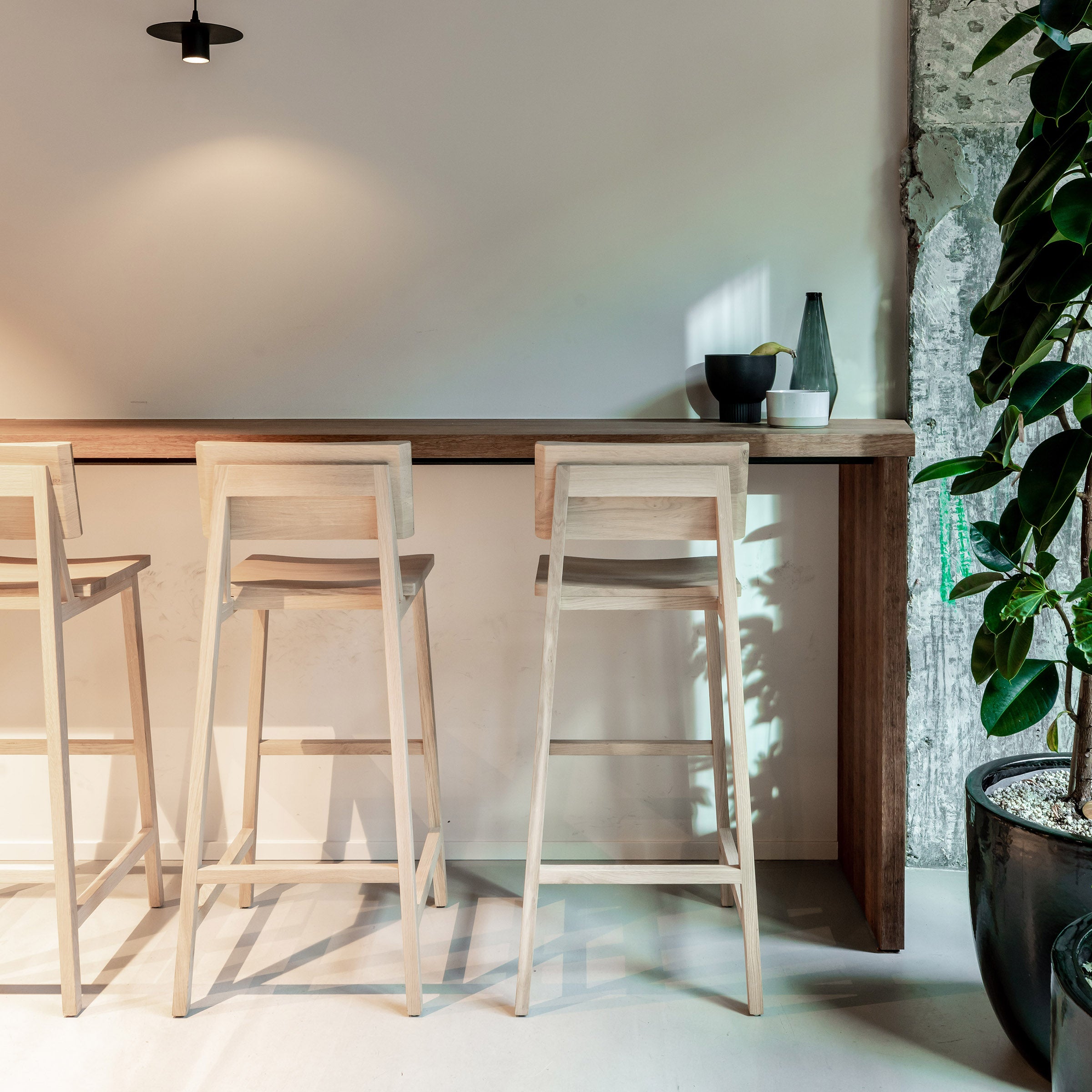 N4 Bar Stool made of varnished oak by Ethnicraft with a minimalist design next to a wooden counter in a modern space.