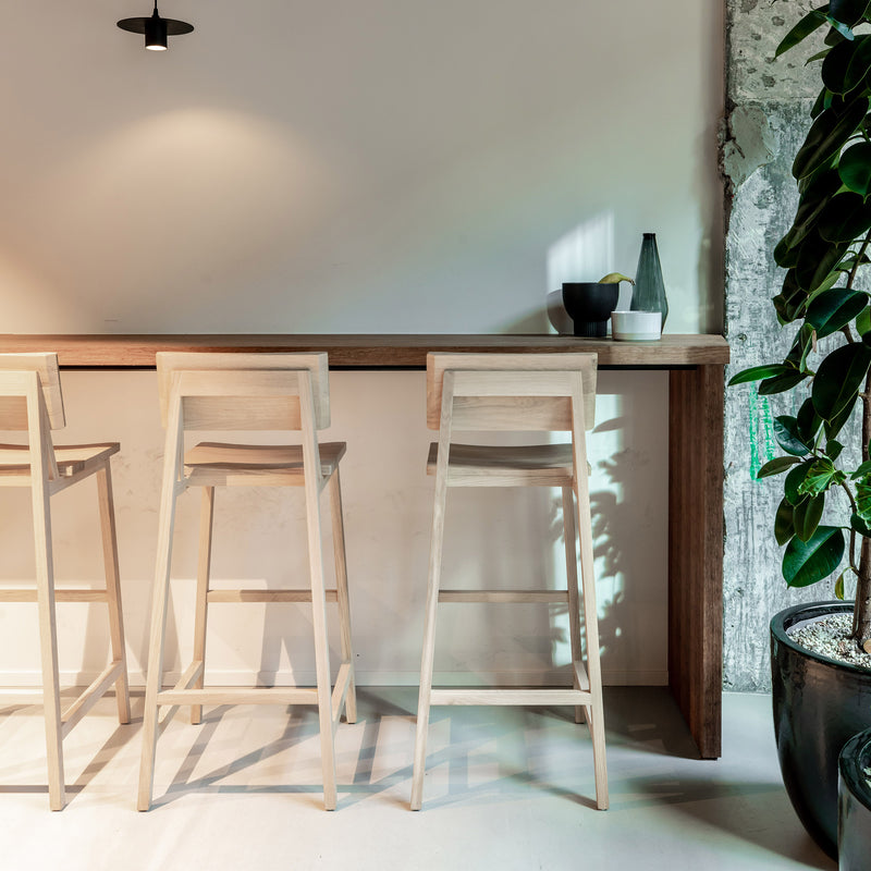 N4 Bar Stool made of varnished oak by Ethnicraft with a minimalist design next to a wooden counter in a modern space.