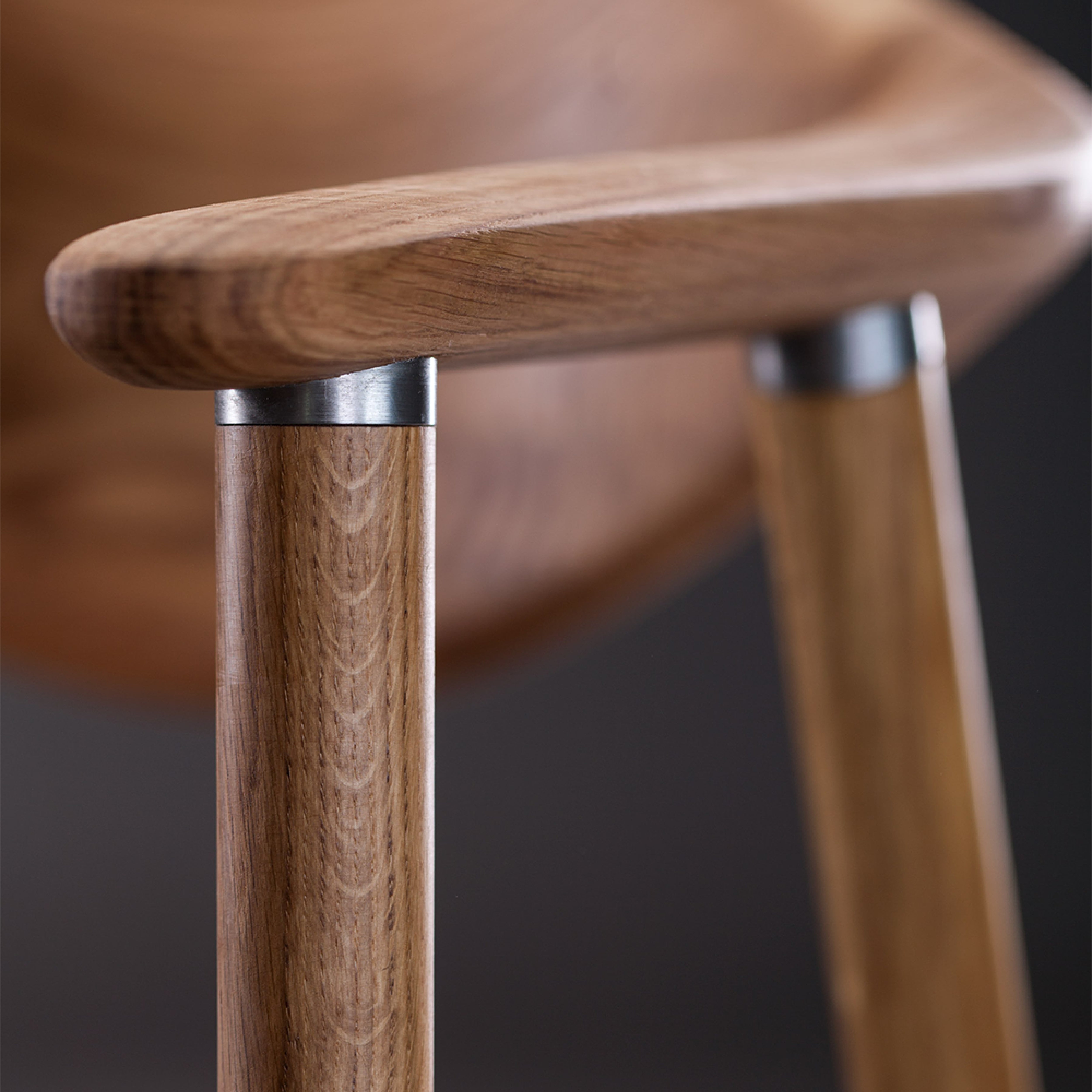 Close-up of the NARU Chair Upholstered Seat by Artisan, with a focus on its minimalist design. Crafted from solid wood, it features smooth, curved armrests and cylindrical legs with metal connectors, finished in natural oils to highlight its craftsmanship and beautiful wood grain.