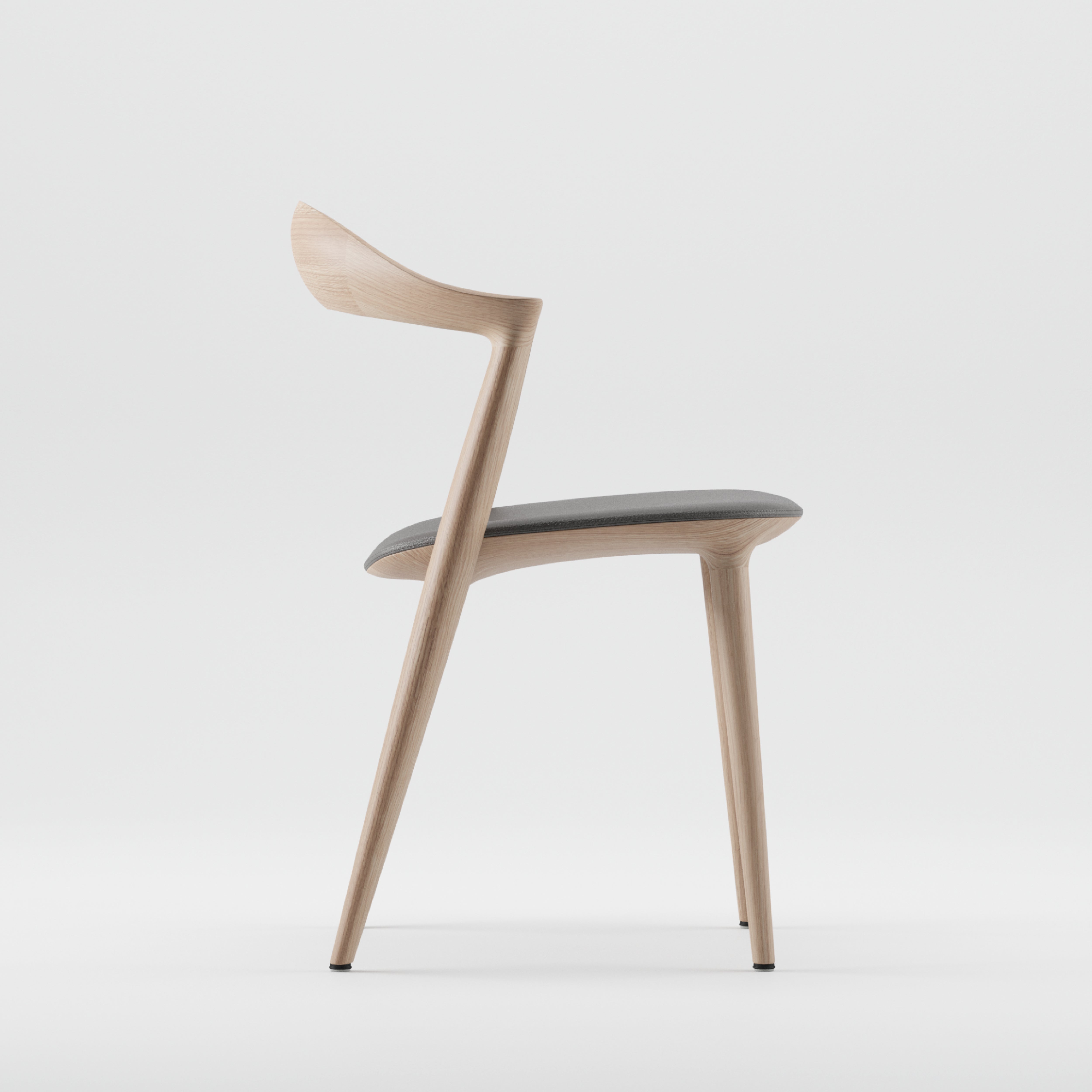 Side view of the Addo Chair by Artisan, a modern piece crafted from solid wood. It features a curved backrest, dark cushioned seat, tapered legs, and minimalist design. Made with eco-friendly materials against a plain light background.