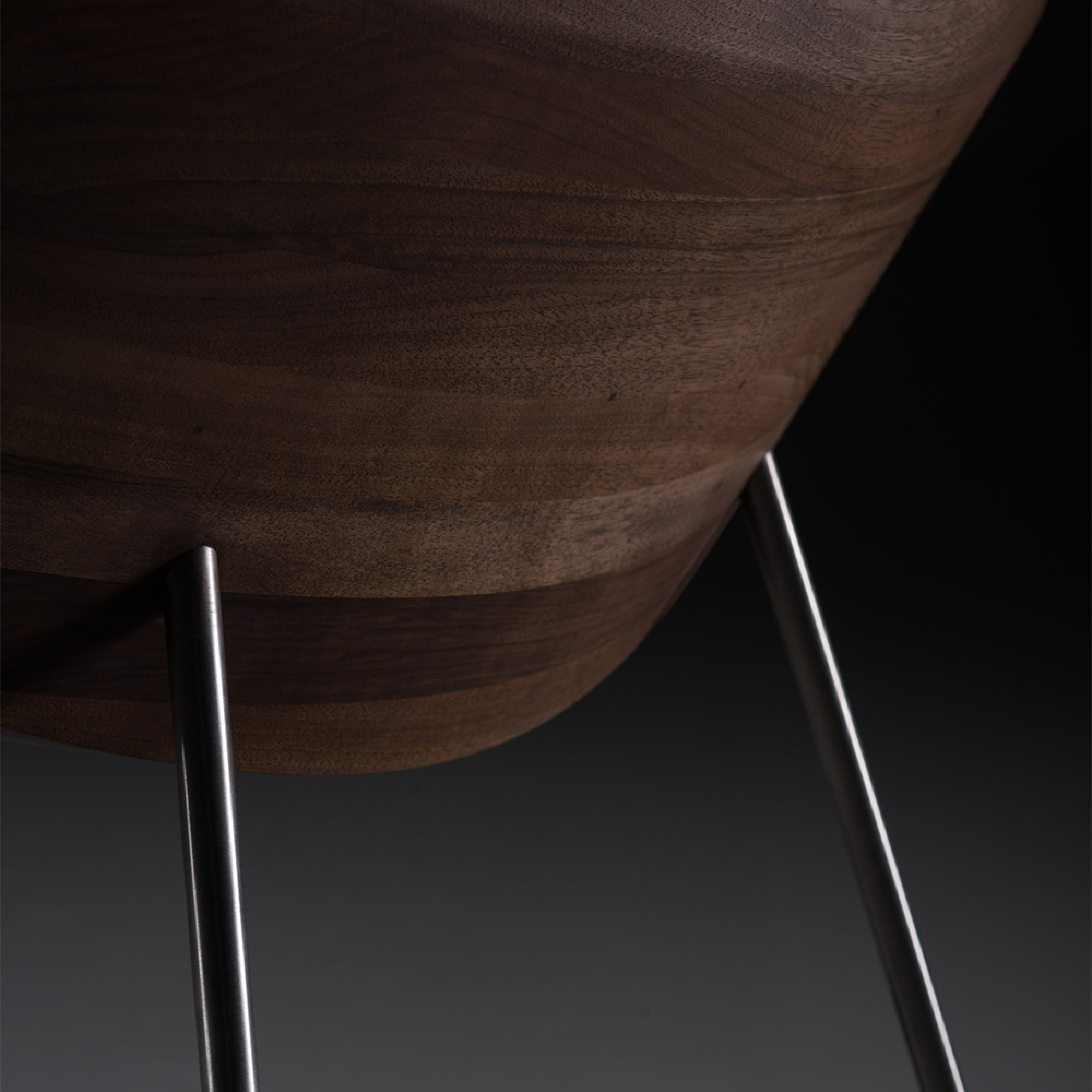 The Artisan CHUNK Chair features a solid wood seat with sleek metal legs. Natural oils enhance the grain, emphasizing the smooth, curved design against a dark background, making it environmentally friendly.