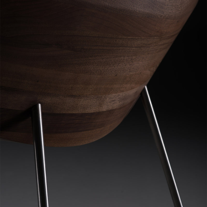 The Artisan CHUNK Chair features a solid wood seat with sleek metal legs. Natural oils enhance the grain, emphasizing the smooth, curved design against a dark background, making it environmentally friendly.