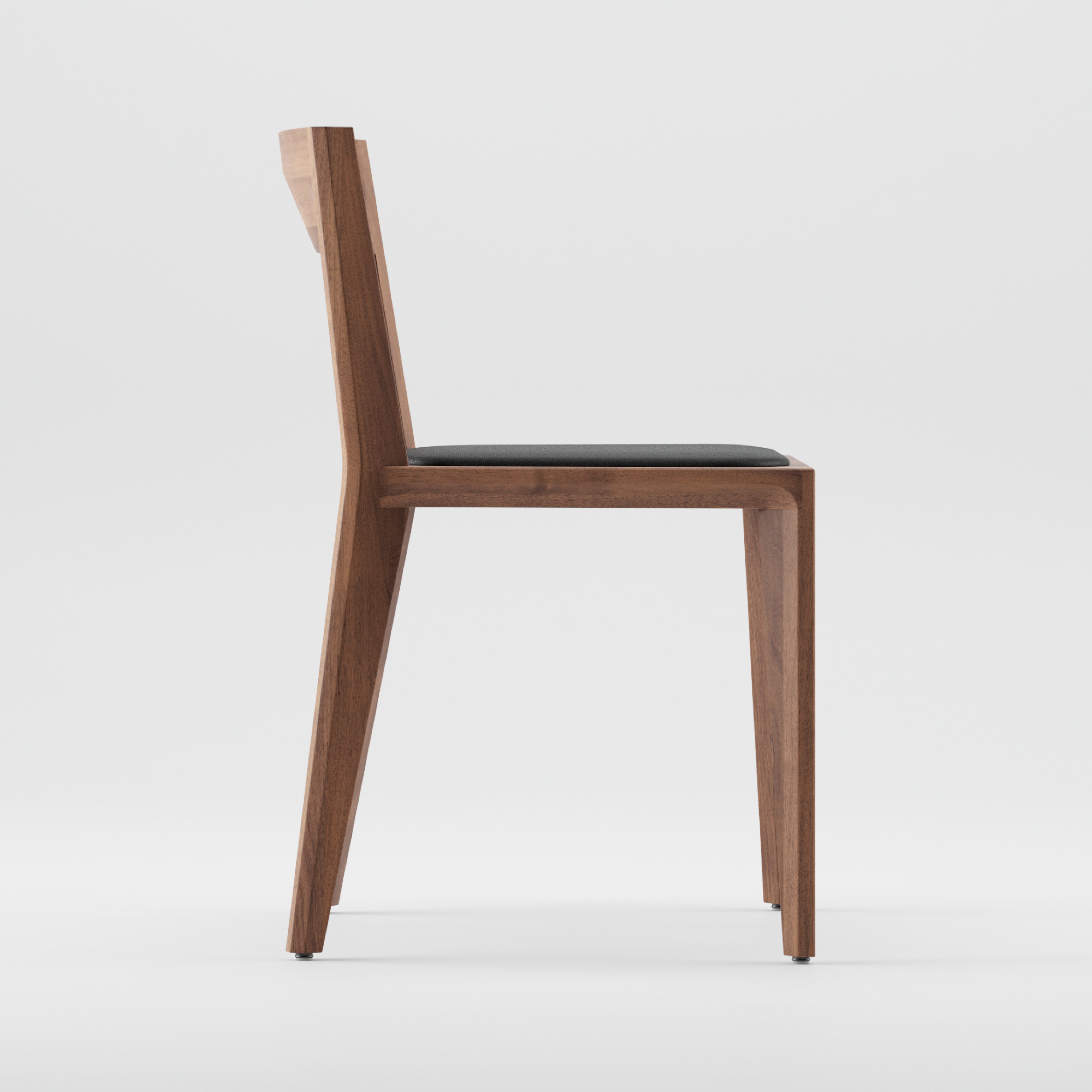 Side view of the HANNY Chair Upholstered by Artisan showcases a modern design crafted from solid wood, coated in natural oils. The chair features a sleek look with a dark cushion seat and slightly reclined backrest against a plain white background.