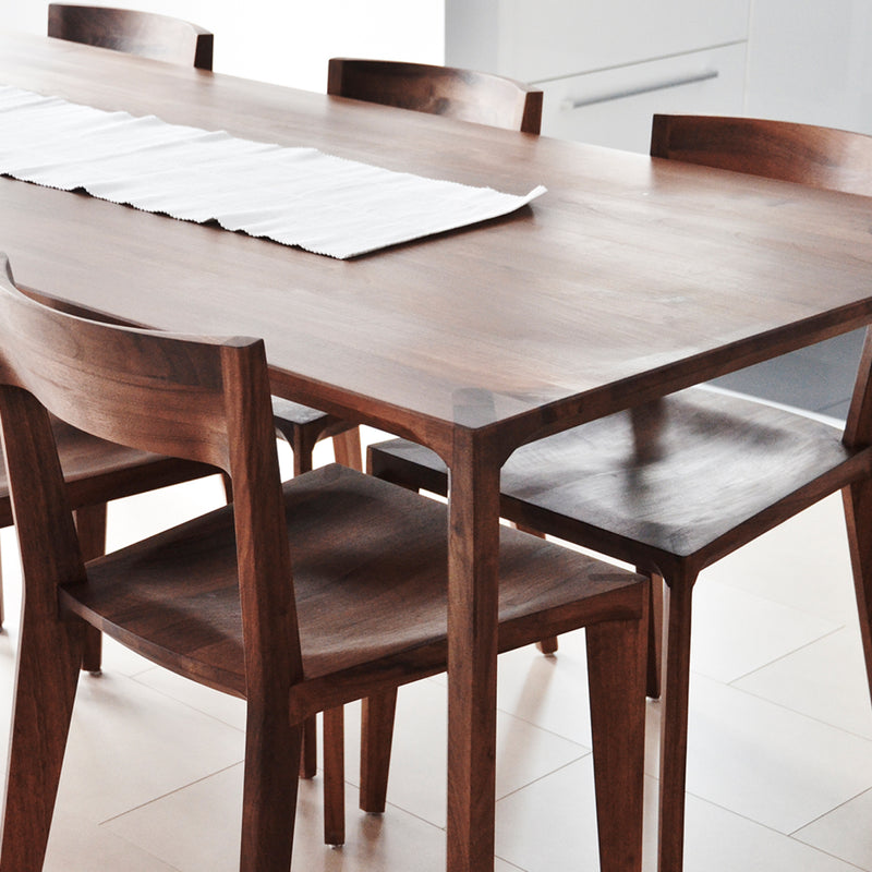 A minimalist dining area is enhanced by a solid wood table with four Artisan HANNY chairs. A white cloth runner adorns the table, and the natural light highlights the clean, modern atmosphere, perfectly showcasing the sustainable materials integrated into the design.
