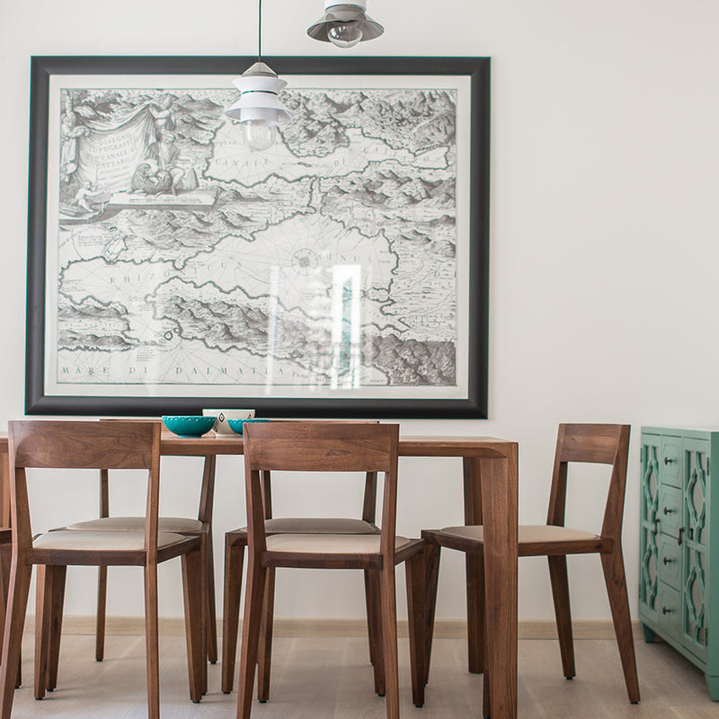 The dining area includes an Artisan solid wood table and four HANNY chairs on a light floor, with a large framed vintage map adorning the white wall. A mint green sideboard showcases teal bowls, while eco-friendly pendant lights cast a warm glow.