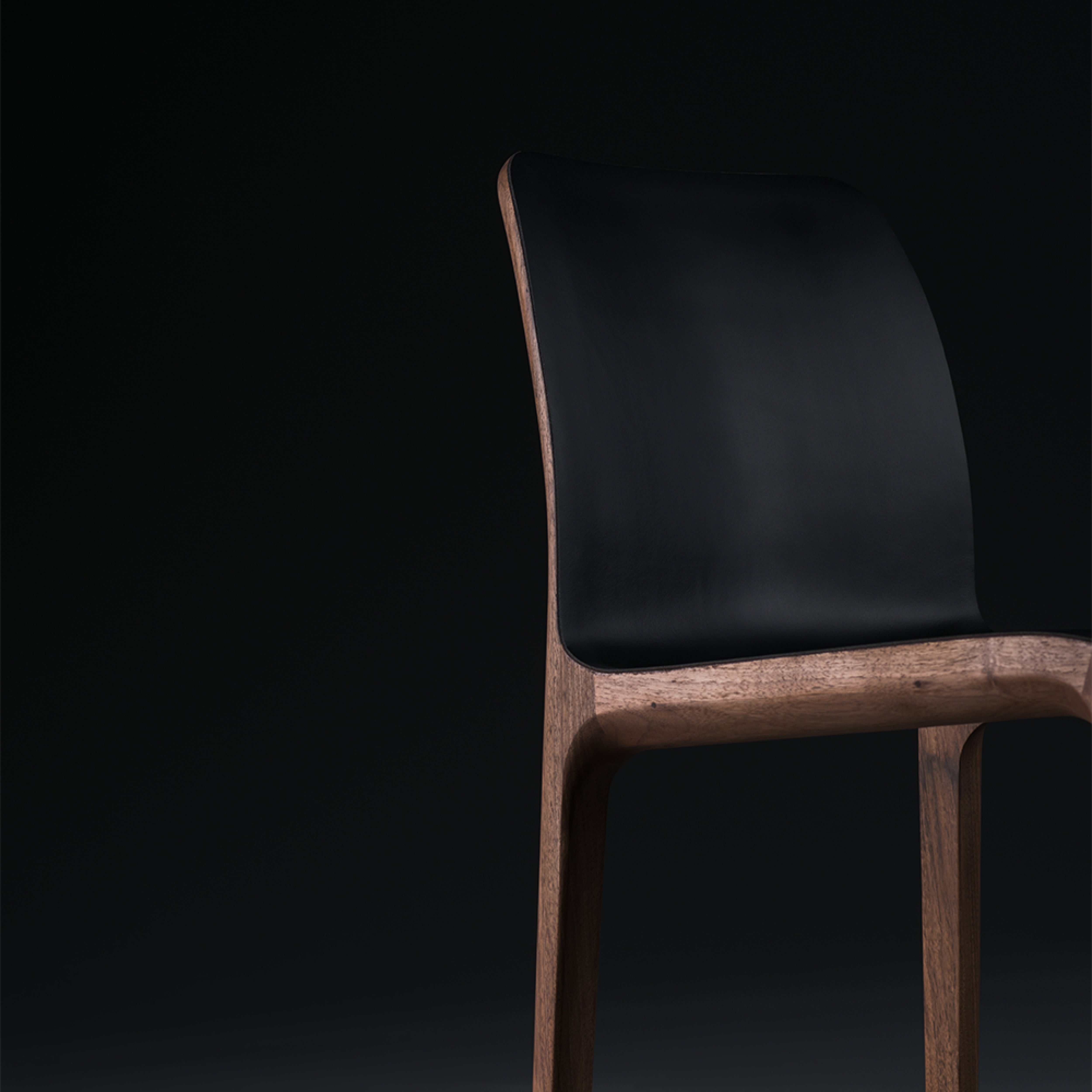 The INVITO Barstool by Artisan is a minimalist wooden chair with a sleek black seat, set against a dark background. Its modern design highlights a curved backrest and solid wood finish.