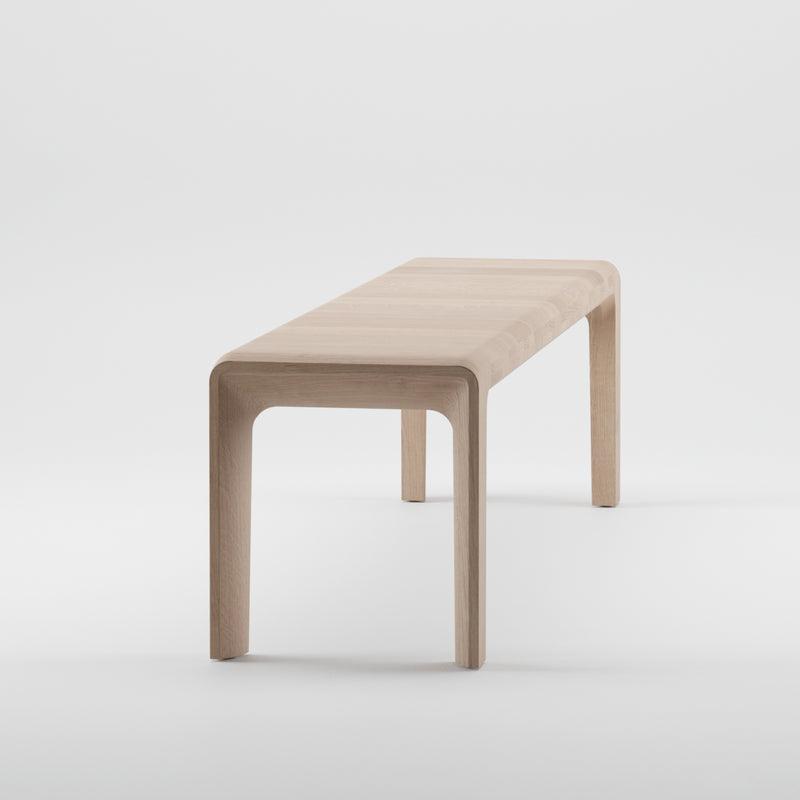 The INVITO Bench by Artisan is a minimalist piece crafted from solid wood with a light natural finish and enhanced with natural oils. It has a smooth rectangular seat supported by four legs, offering a sleek modern design against a plain white background.