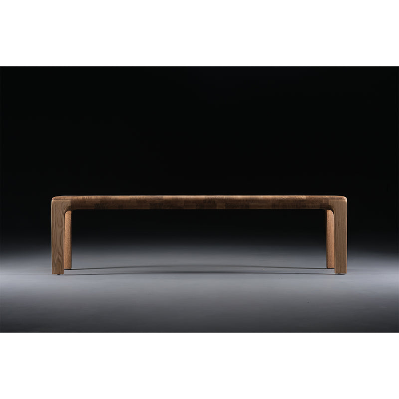 The INVITO Bench by Artisan, a minimalist piece crafted from solid wood and treated with natural oils, stands against a black background, elegantly lit from above to emphasize its sleek surface and clean lines.