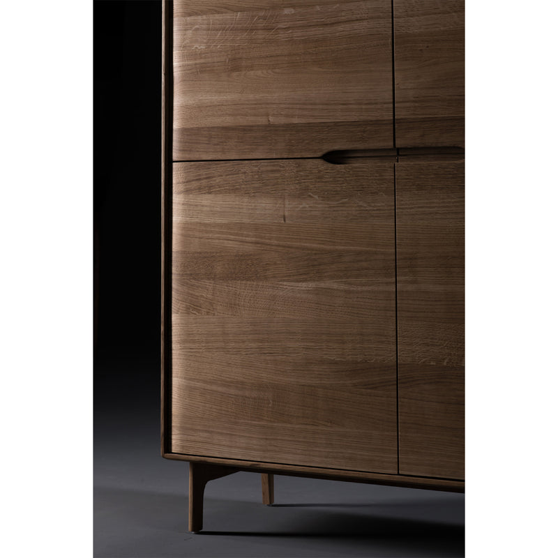 The INVITO Highboard by Artisan features a smooth, dark-finished solid wood with minimalist design. Made from eco-friendly materials, it stands on tapered legs against a dark backdrop.