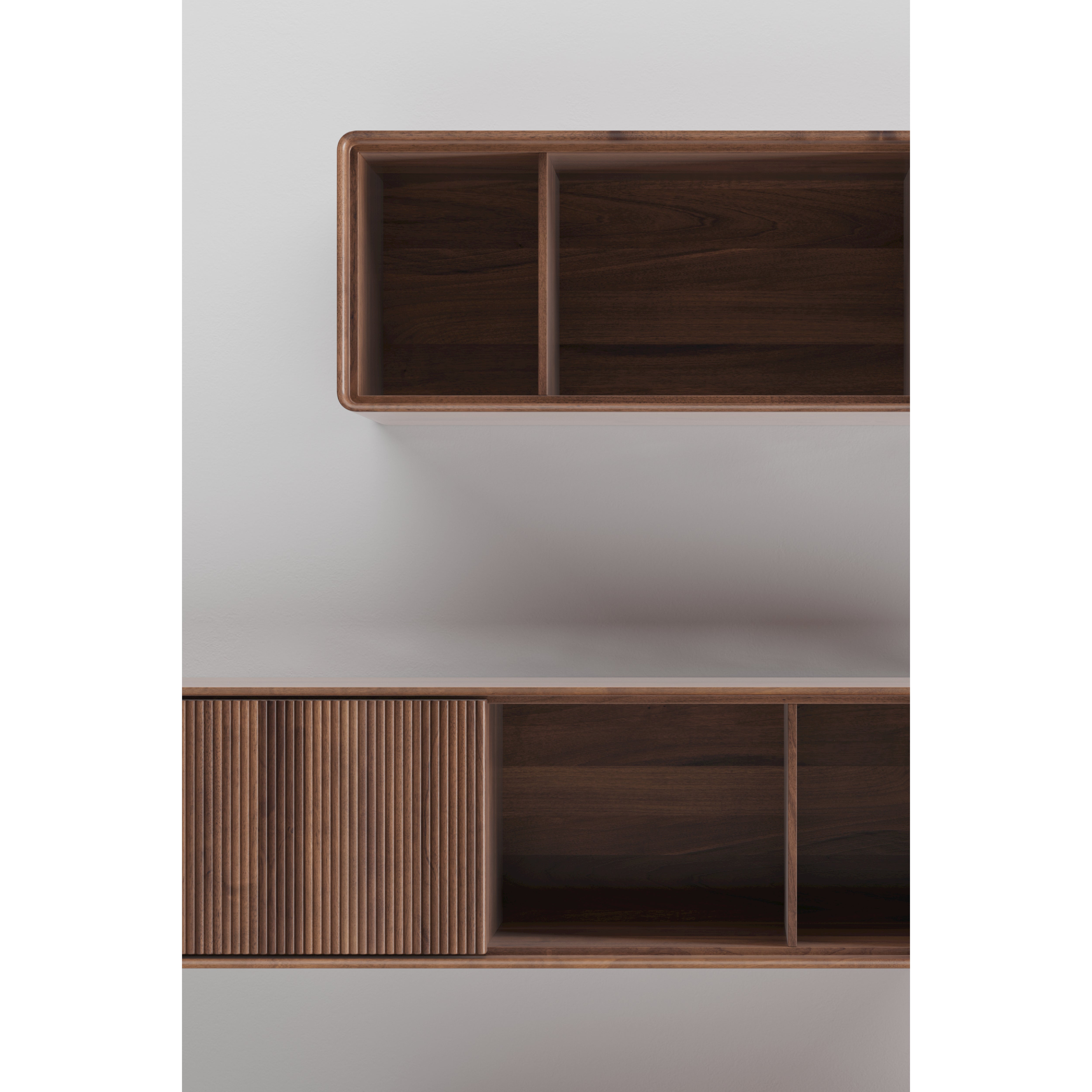 Top view of JANTAR Modular System by Artisan, showcasing elegant, minimalist wooden shelves on a white wall. Crafted from solid wood and finished with natural oils, the upper shelf has two open compartments while the lower one features three sections, including one with a ribbed sliding panel.