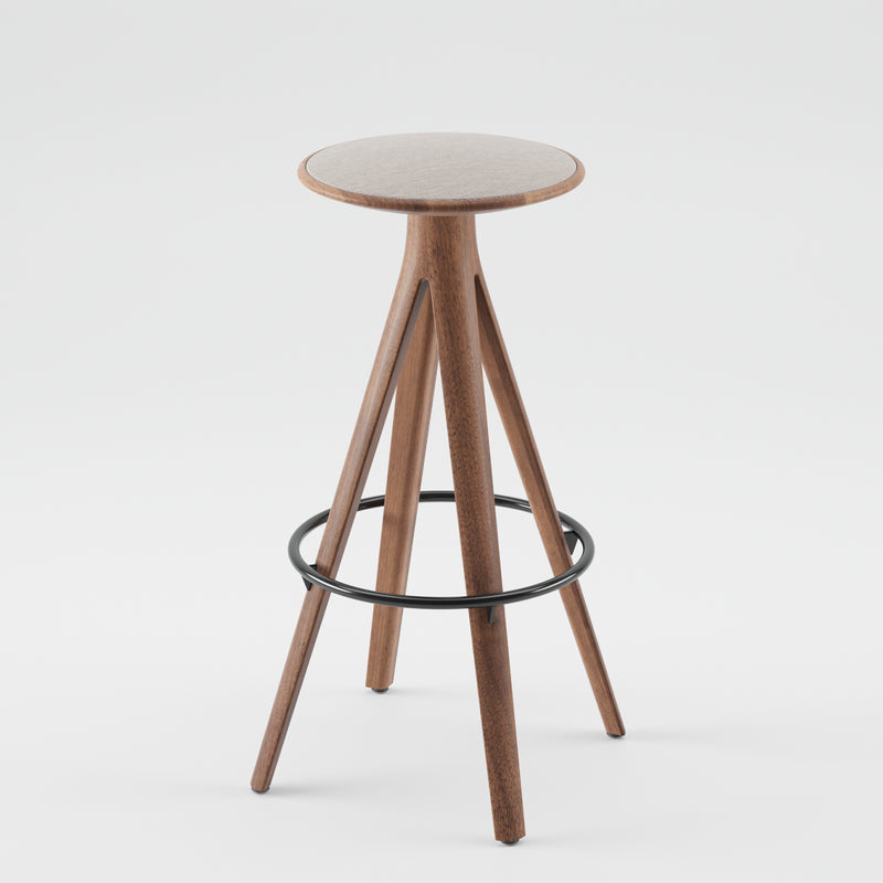 The Artisan KALOTA Barstool boasts a minimalist design with a round, light-colored solid wood seat treated with natural oils, four angled legs, and a black metal circular footrest, offering an eco-friendly seating option.