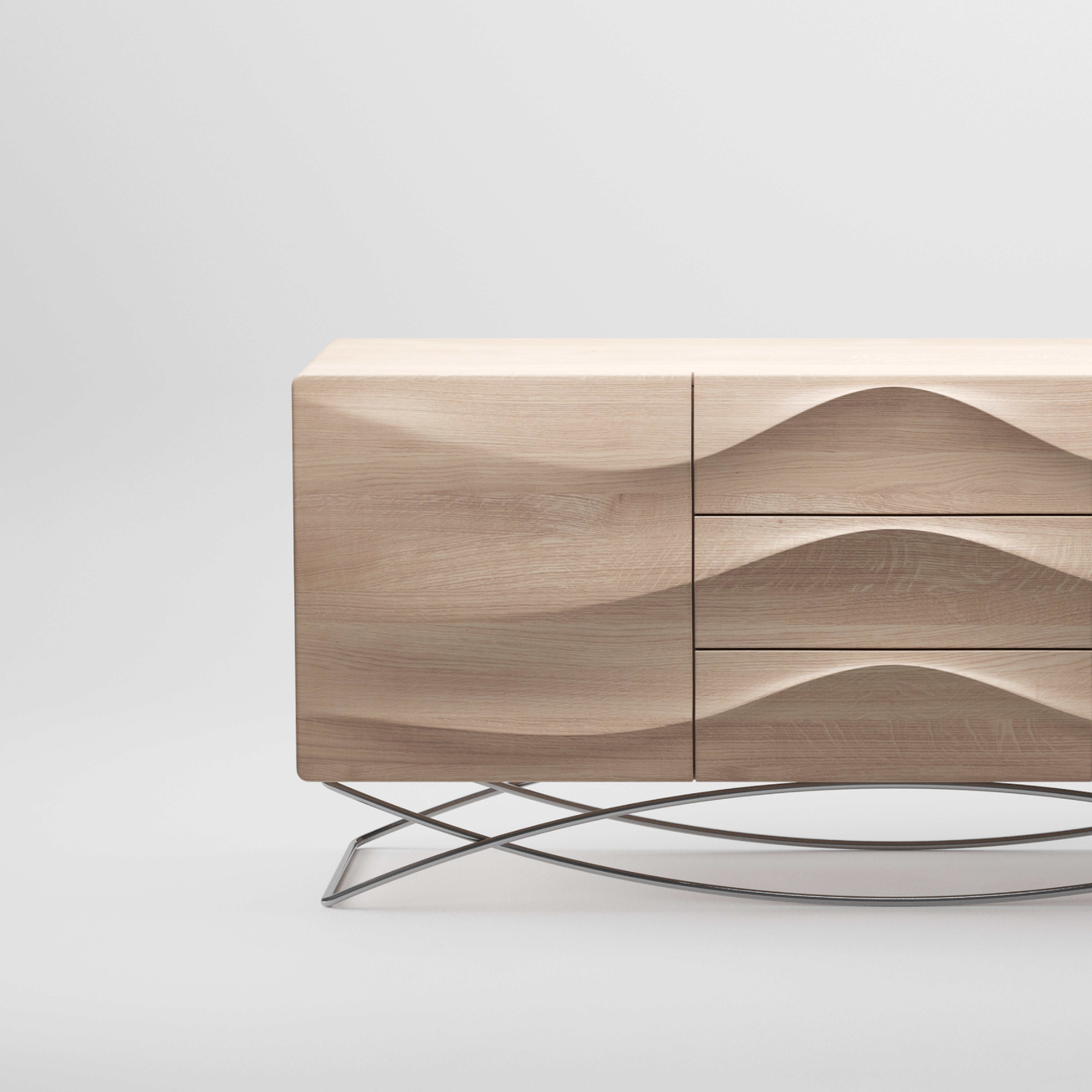 The LASTA Sideboard by Artisan is a modern piece crafted from solid wood with a wavy front texture, featuring three drawers and one cabinet door. It stands on a sleek, curved metal base against a light gray background and is treated with natural oils for an eco-friendly finish.
