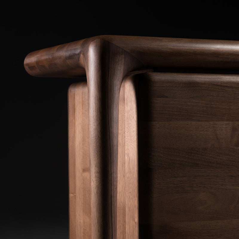The LASTA Sideboard by Artisan features intricate craftsmanship, with smooth curves and joints in solid wood. Its dark, rich finish accentuates its elegant design, emphasizing organic beauty against a black background.
