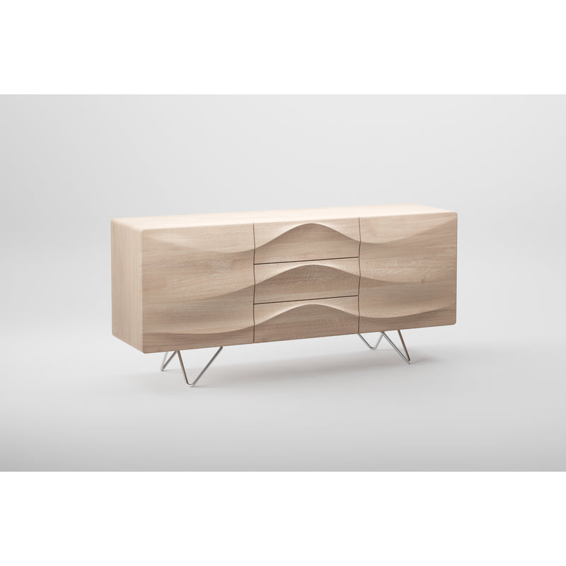 The Artisan LASTA Sideboard is a modern light wood piece crafted from solid wood and finished with natural oils. It features a wavy, sculpted front with three center drawers, two side cabinets, and sleek metal legs, all set against a plain white background.