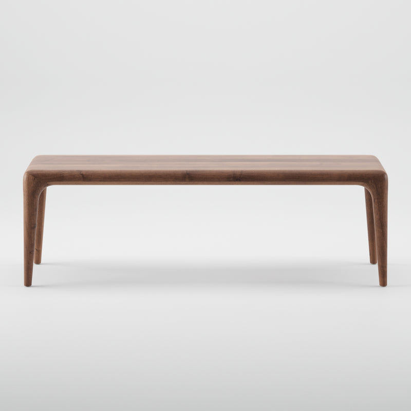 The LATUS Bench by Artisan is a minimalist wooden bench crafted from solid wood, featuring a smooth surface and tapered legs. Set against a plain white background, its elegant design showcases the natural wood grain, finished with eco-friendly natural oils.