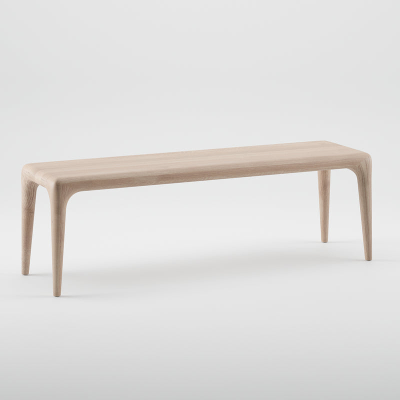 The LATUS Bench by Artisan is a minimalist piece crafted from solid wood. It features four slender, tapered legs and is enhanced with natural oils, showcasing a light, natural wood tone against a plain white background.