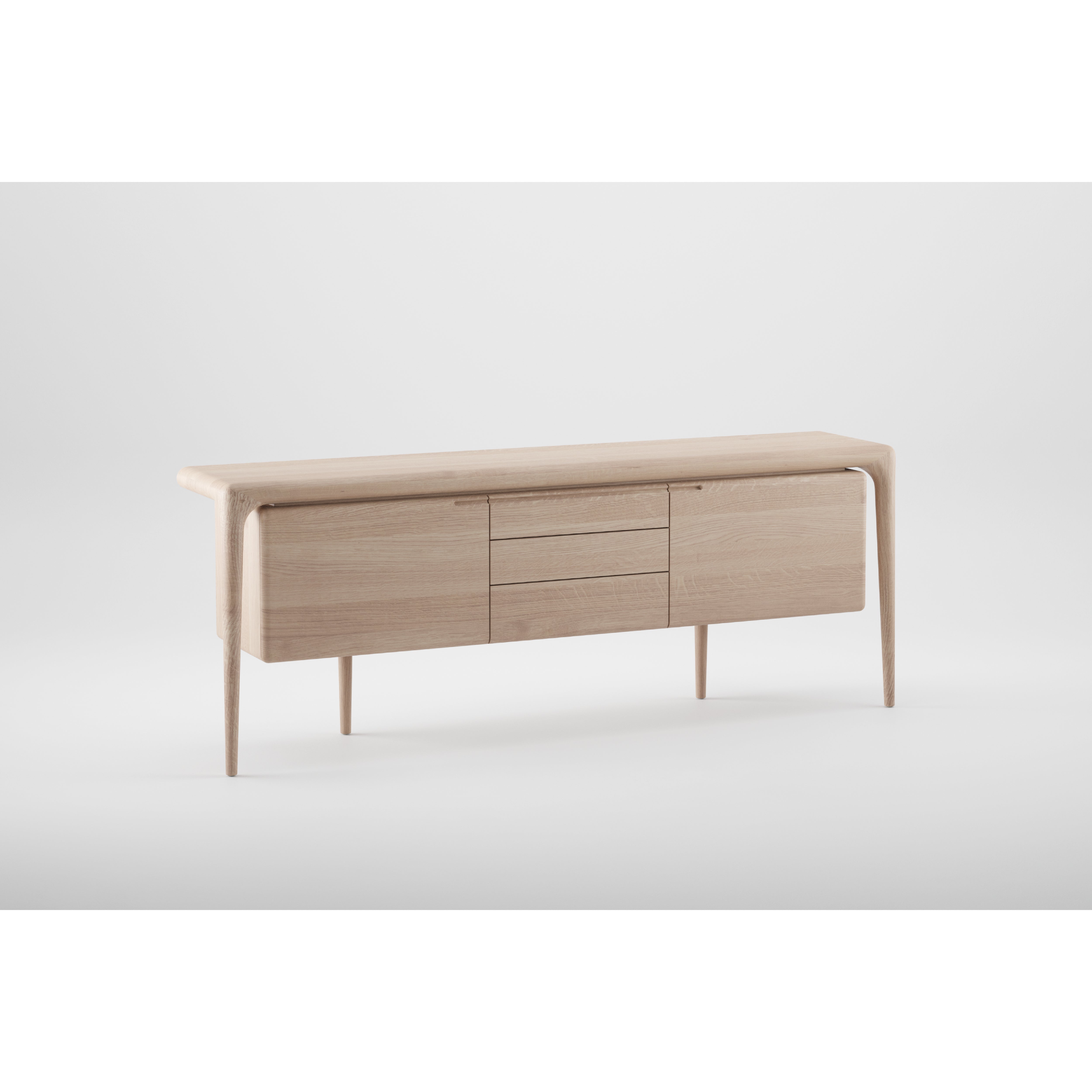 The LATUS Sideboard by Artisan is a minimalist piece crafted from solid wood with a light finish. It boasts a sleek design with a flat top, two side cabinet doors, and three central drawers. Built using eco-friendly materials, its slender legs highlight the modern aesthetic.