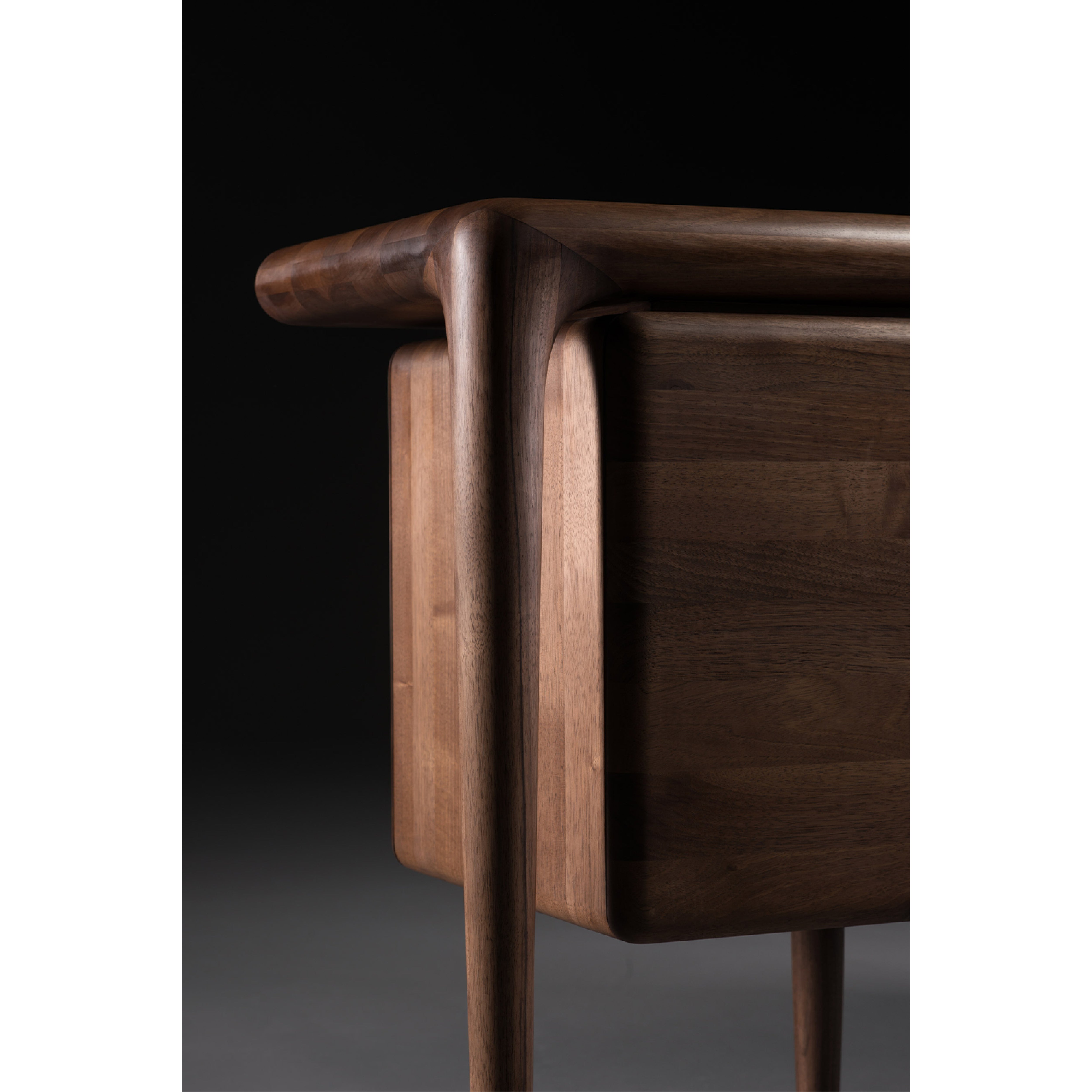 Close-up of the LATUS Sideboard by Artisan, crafted from solid wood. It features smooth, rounded edges with sleek, tapered legs and a natural oil finish, all set against a dark background.