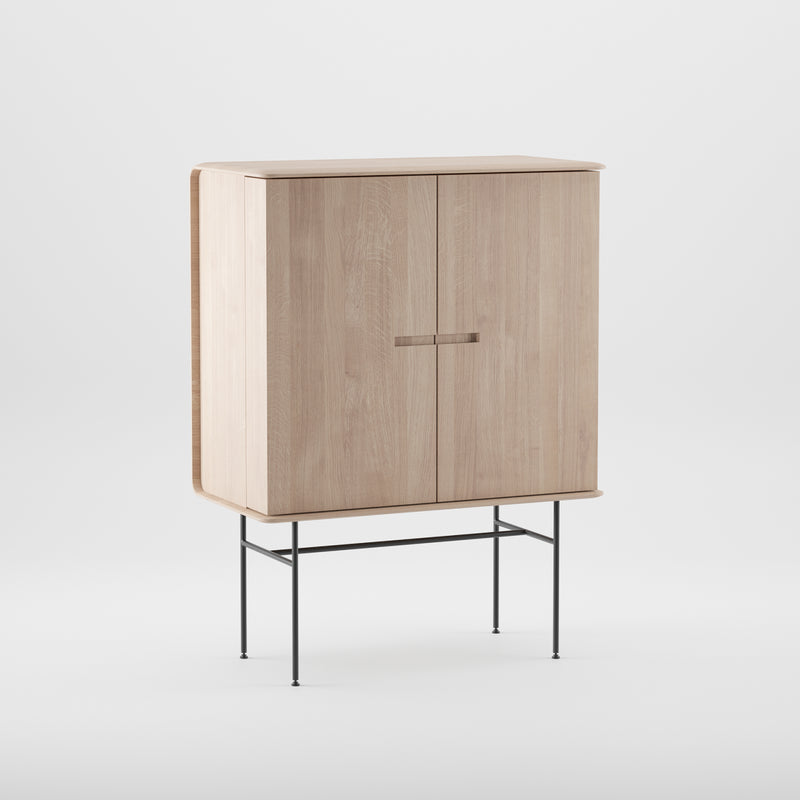 The Leno Bar by Artisan is a wooden cabinet crafted from solid wood with a light finish. It features two doors, sleek metal legs, minimalist design, and subtle handles against a plain white background.