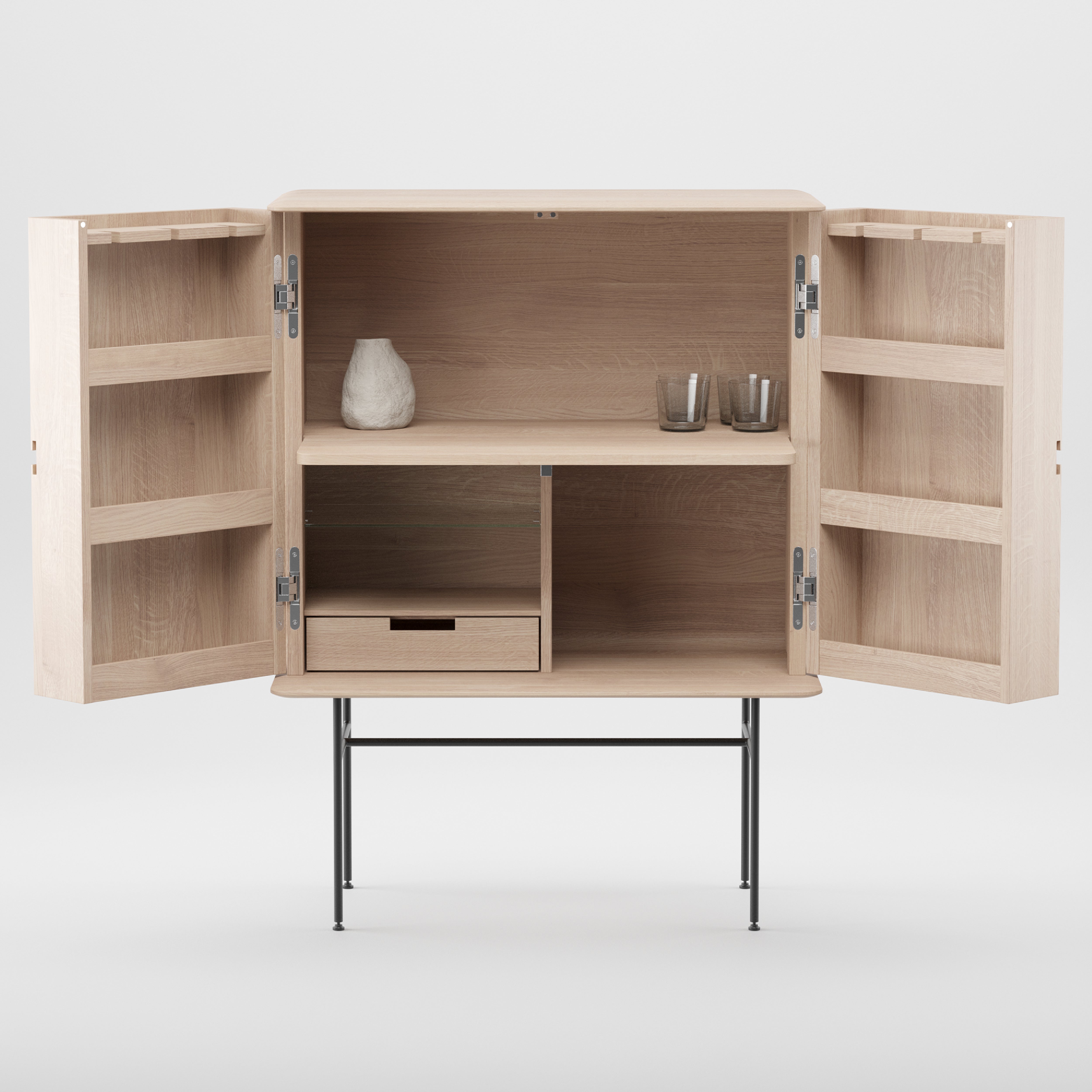 The Leno Bar by Artisan features modern design with light wood, open doors revealing minimalistic shelving adorned with a vase and two glasses. An open shelf complements a closed drawer below. This artisan furniture rests on slim black metal legs.