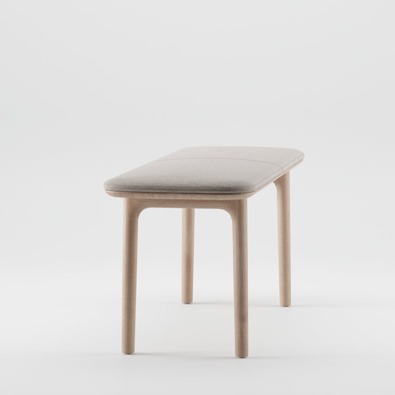 The NEVA Bench by Artisan features a minimalist design with a light beige cushioned seat and four wooden legs, expertly crafted from organic wood. The elegant structure stands out beautifully against a plain white background.