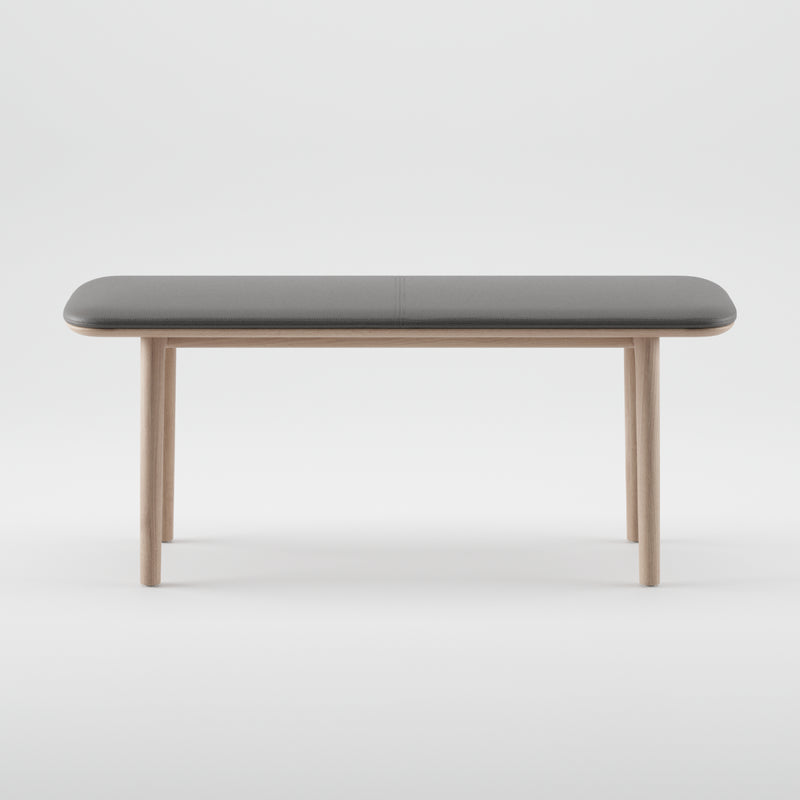 The Artisan NEVA Bench from the Neva collection boasts a minimalist design with a sleek rectangular gray top and light wooden legs, crafted using organic wood forms. It effortlessly blends modern and natural elements against a plain white backdrop.