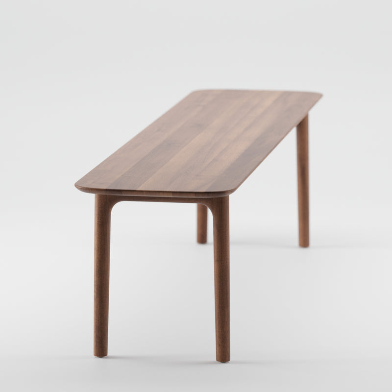 The NEVA Bench by Artisan is a minimalist wooden bench with a rectangular seat and slightly tapered legs, showcasing organic wood forms. It features a smooth, natural wood finish, rounded edges, and is set against a white background.