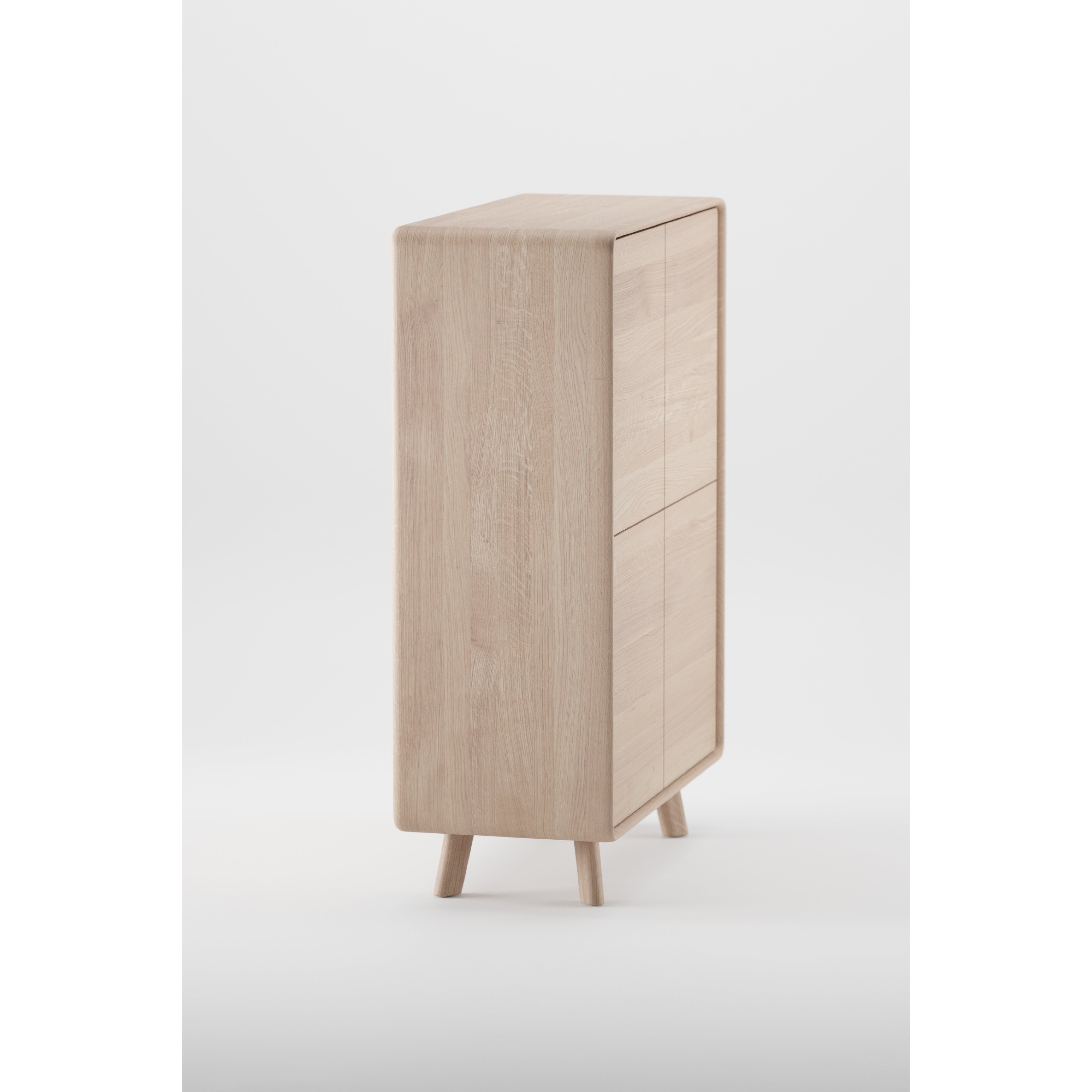 The Artisan NEVA Highboard is a tall cabinet with a minimalist design, made of light wood with natural finishes. It features two doors, stands on four angled legs, and showcases a sleek, smooth texture that highlights its modern rectangular shape against a plain white backdrop.